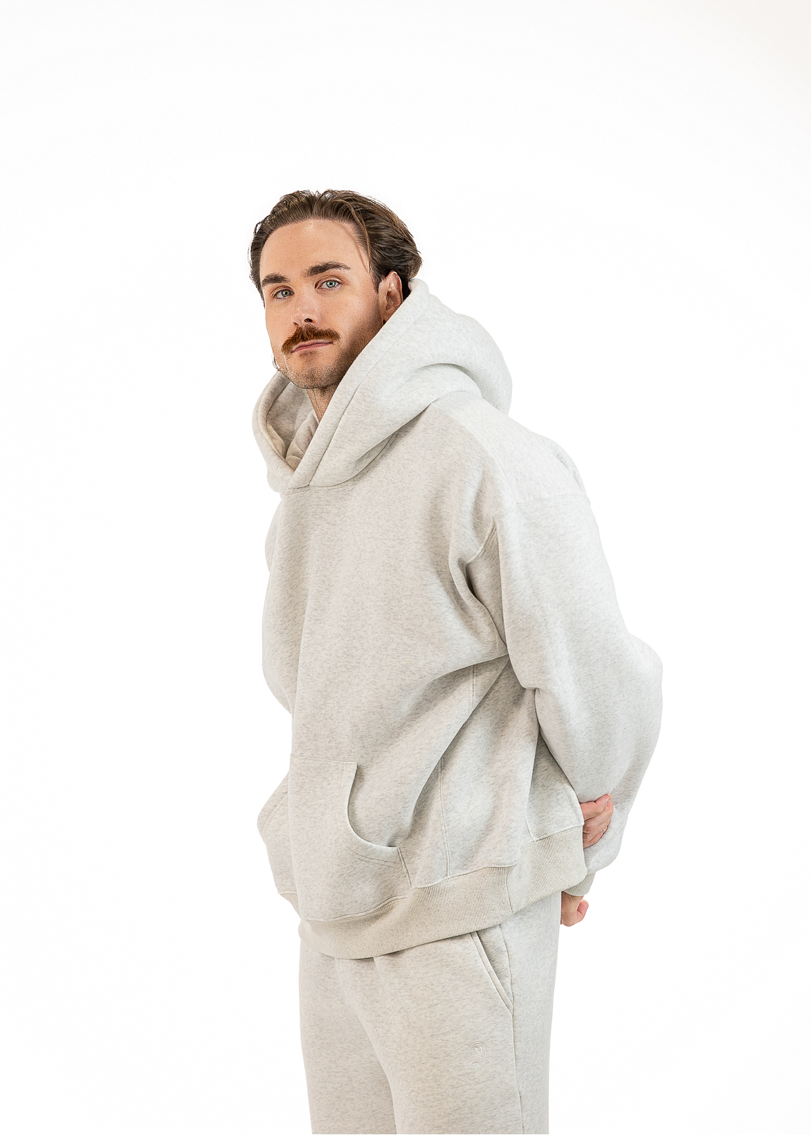 A man wearing a light gray heathered hoodie and matching sweatpants, standing against a solid white background.