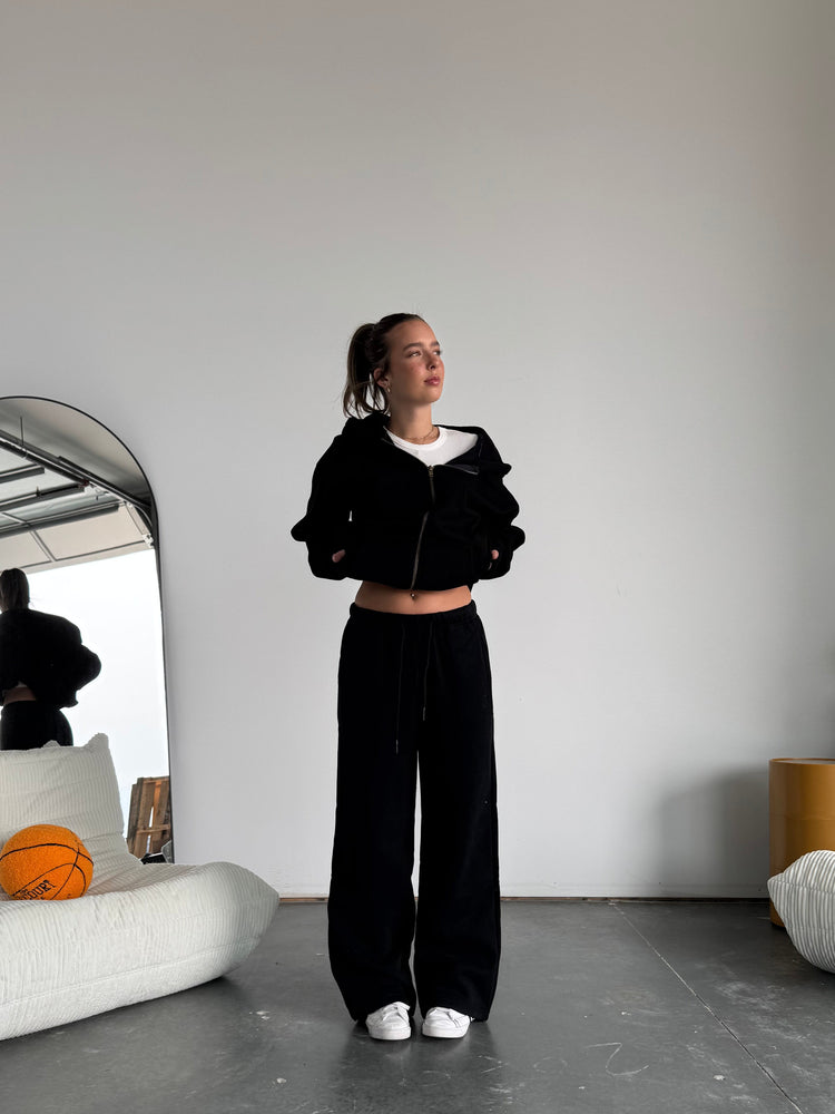 Person wearing a black outfit standing on a skateboard with a mirror reflection.