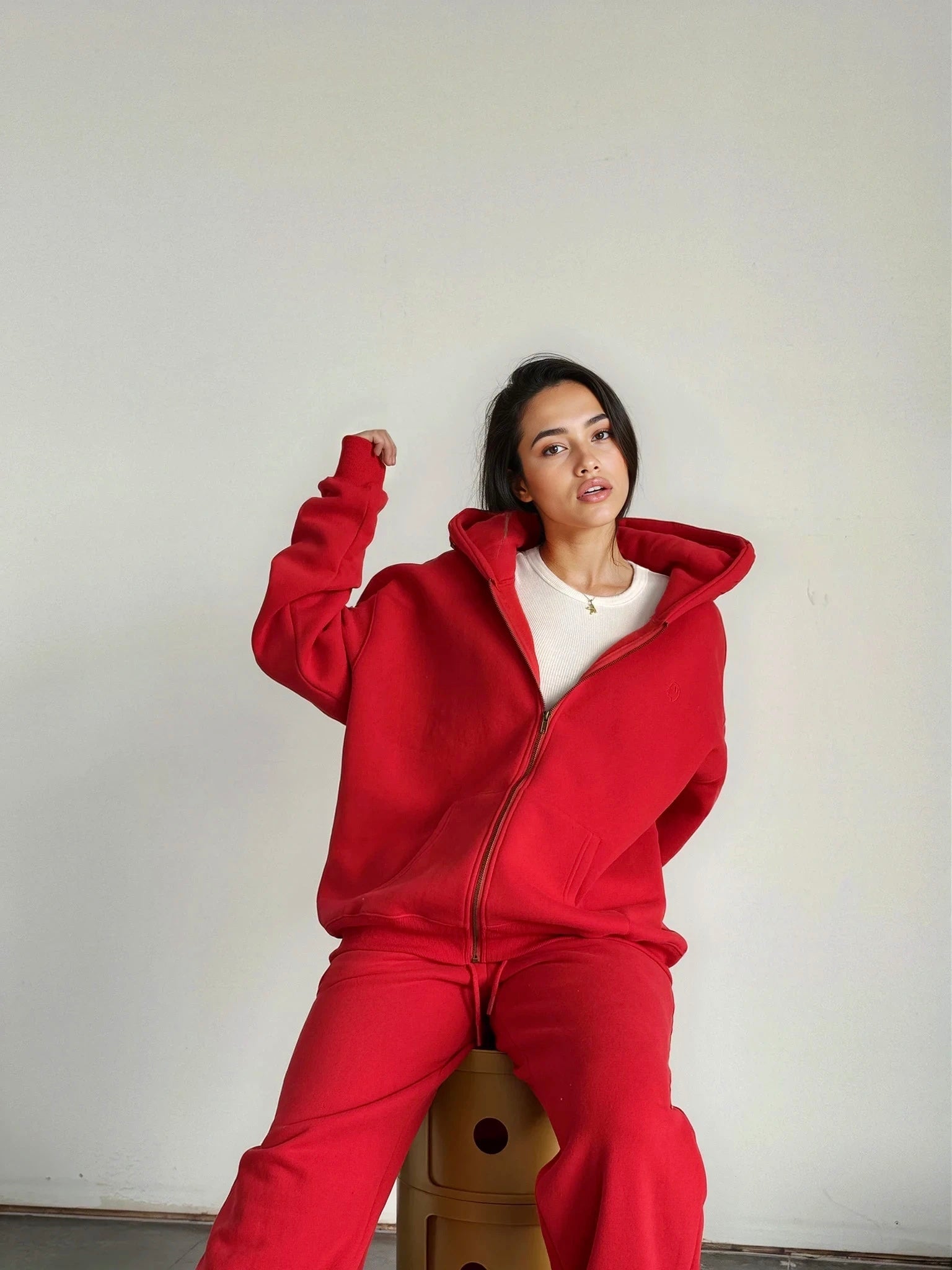 Person wearing a red tracksuit sitting on a wooden stool against a plain background