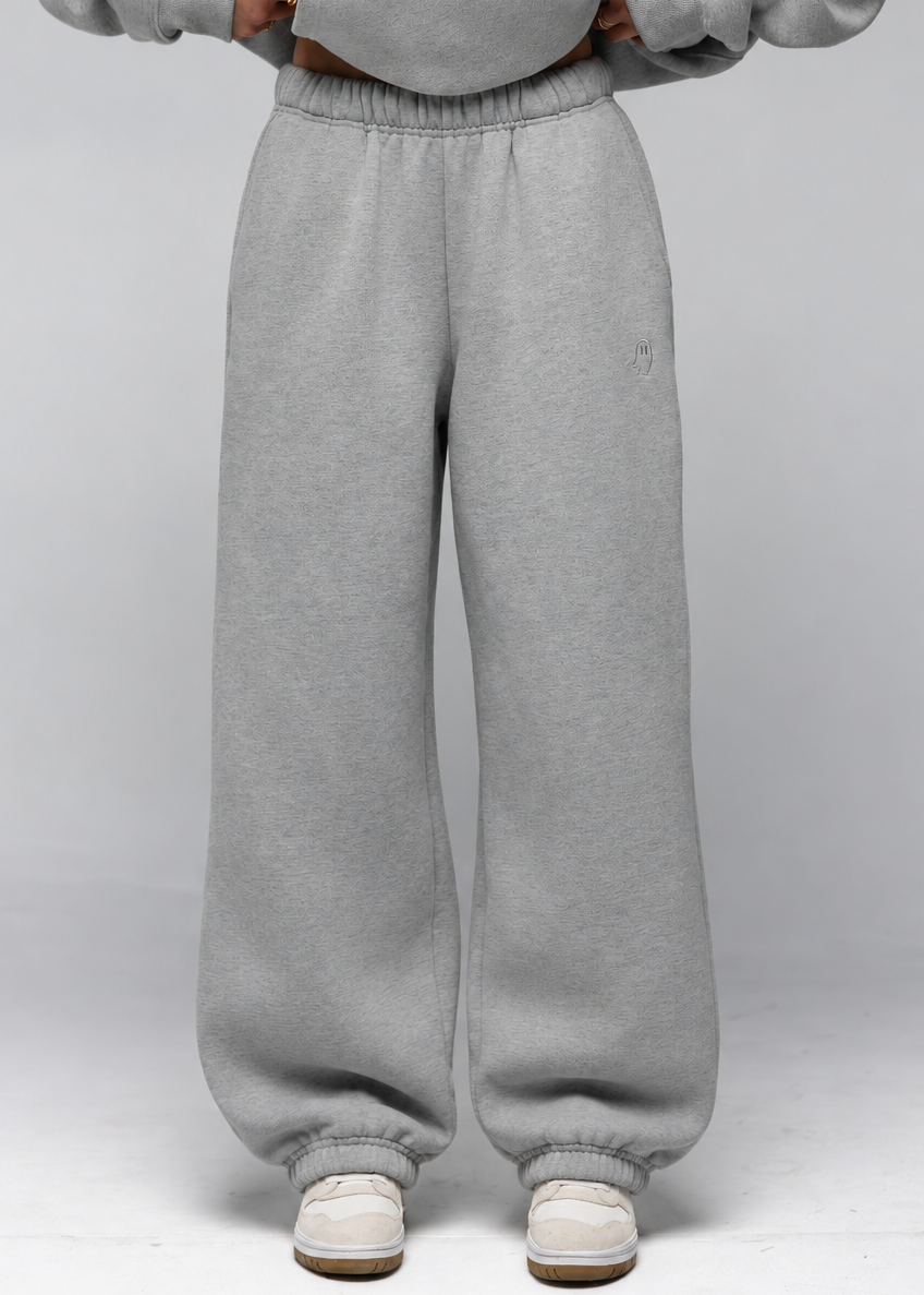 A person wearing light gray sweatpants and a matching gray sweatshirt, standing against a light gray studio background. The photo is cropped from the chest down, showing the full length of the sweatpants and white sneakers.