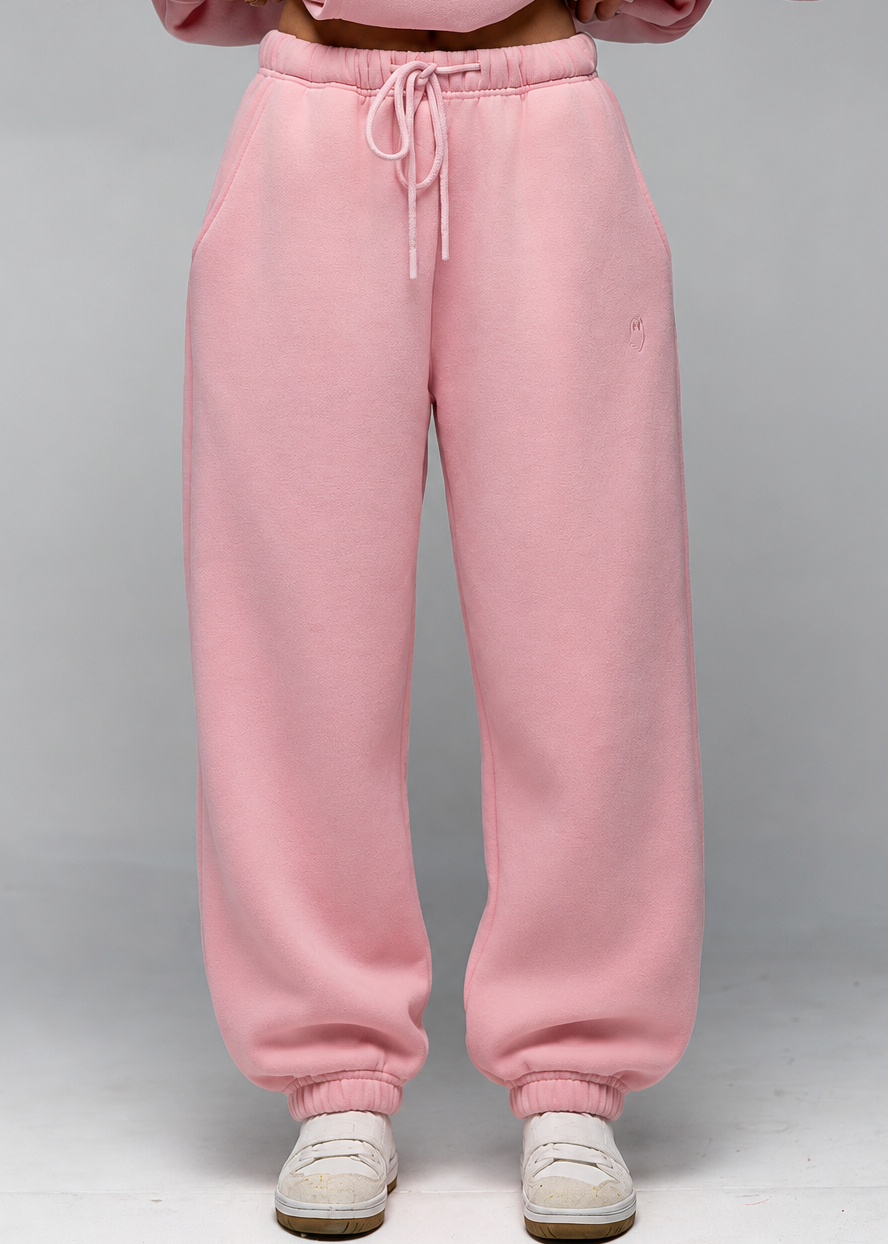 A person wearing loose pink sweatpants with a drawstring waist and white sneakers, shown from the chest down against a light gray studio background.