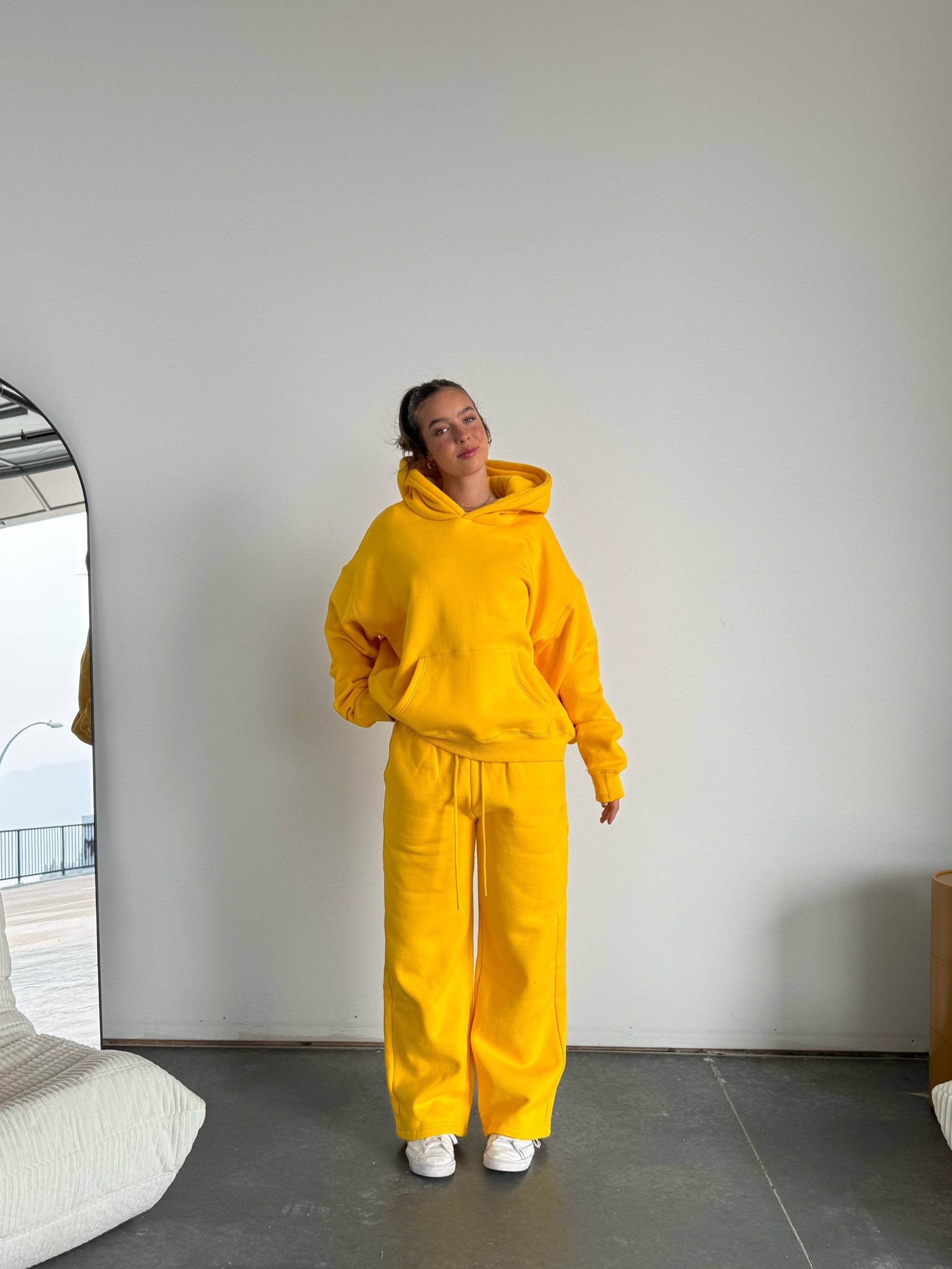 Person wearing a yellow hoodie and pants standing in a modern room with a white wall and gray floor.