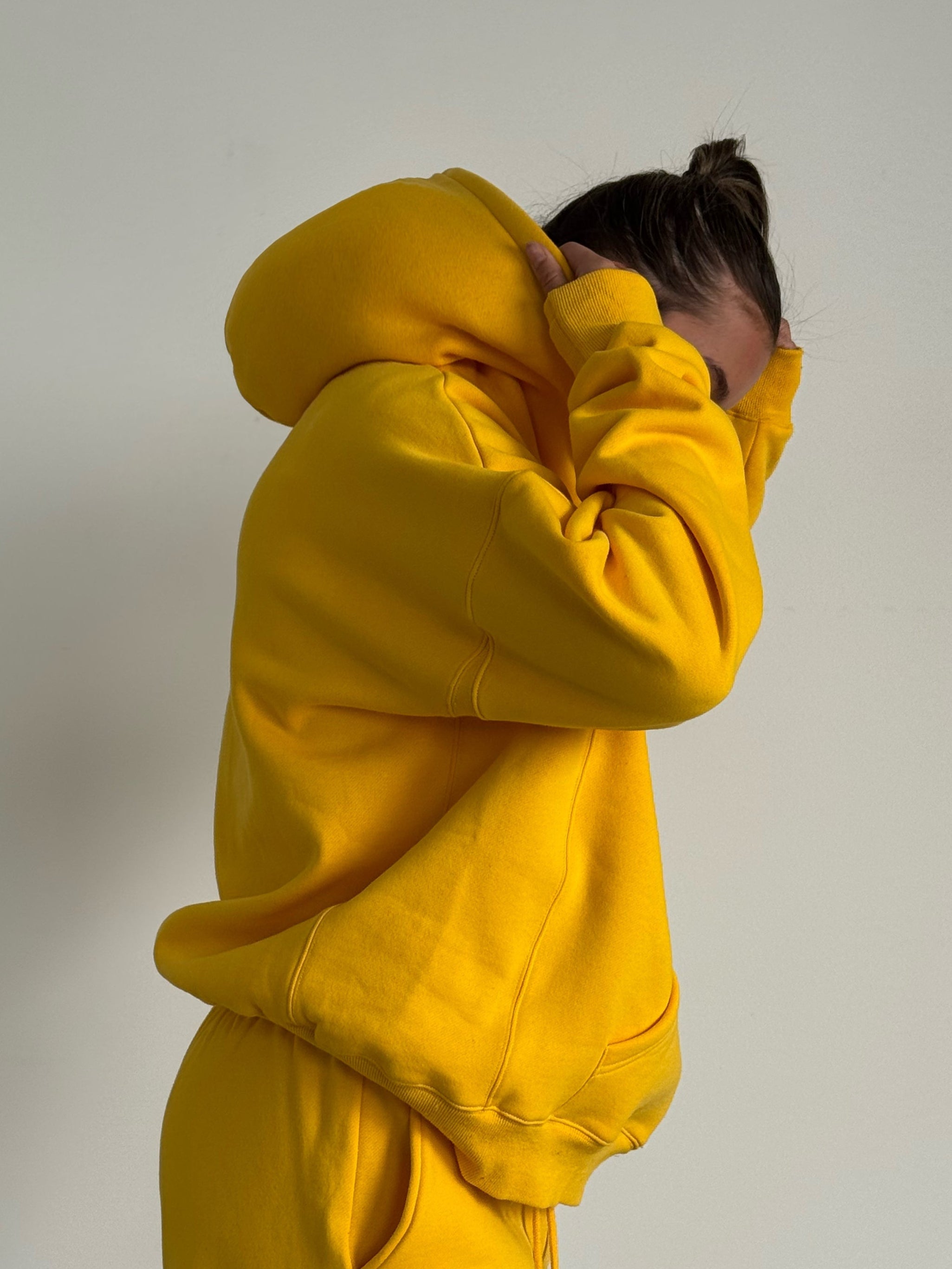 Person wearing a yellow hoodie and pants against a plain background