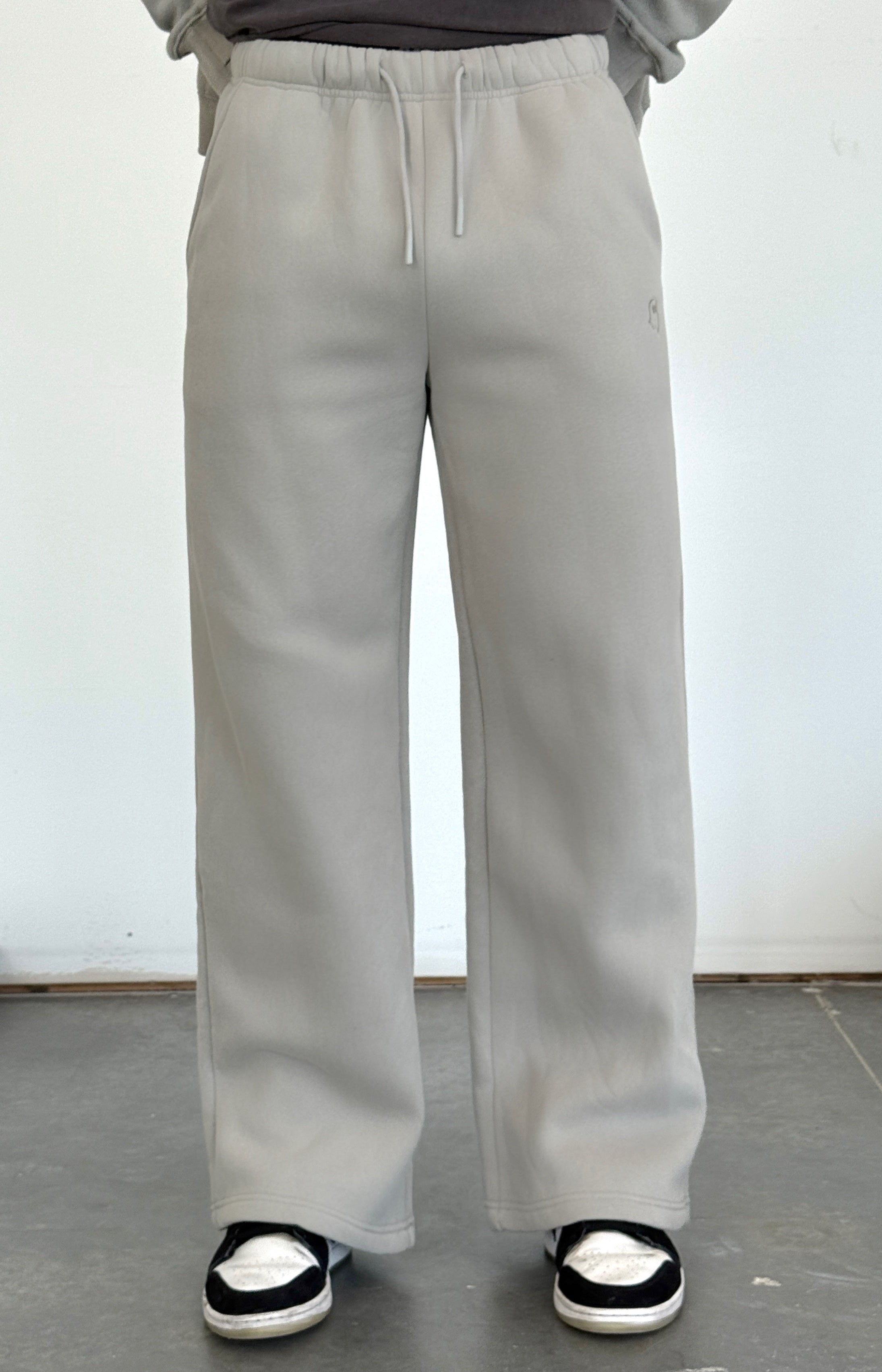 Person wearing light gray pants and a dark shirt against a white wall.