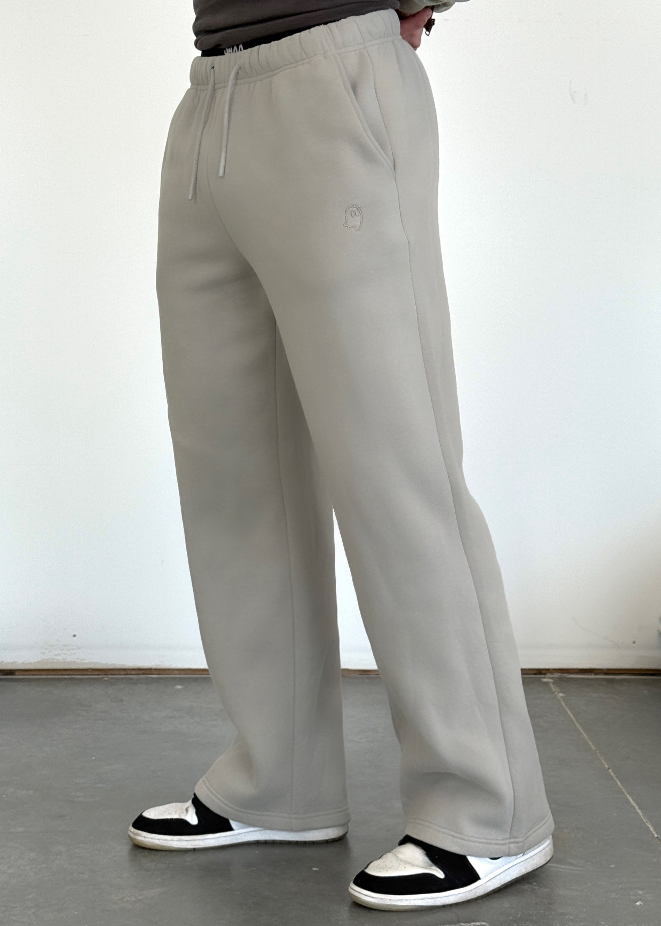 Person wearing light gray pants and black and white shoes on a plain floor.