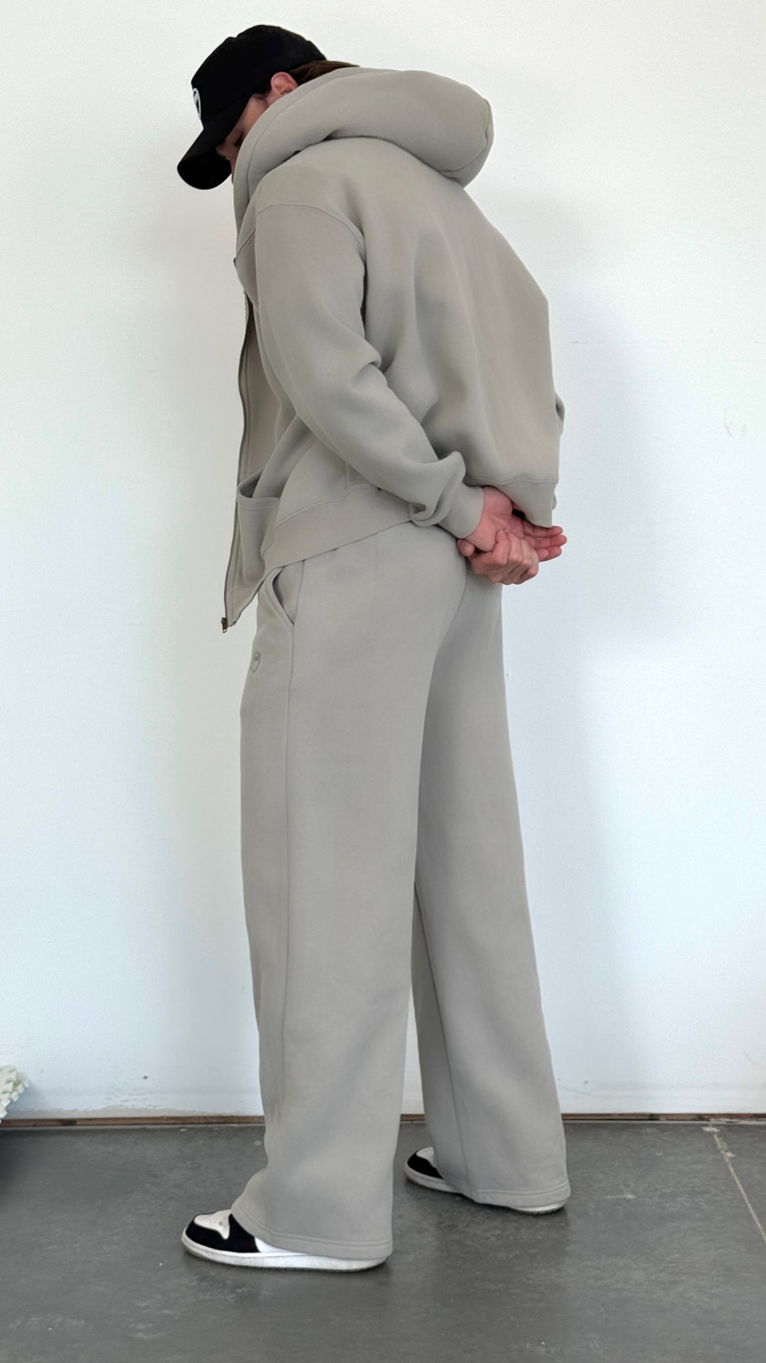 Person wearing a gray tracksuit standing against a white wall.