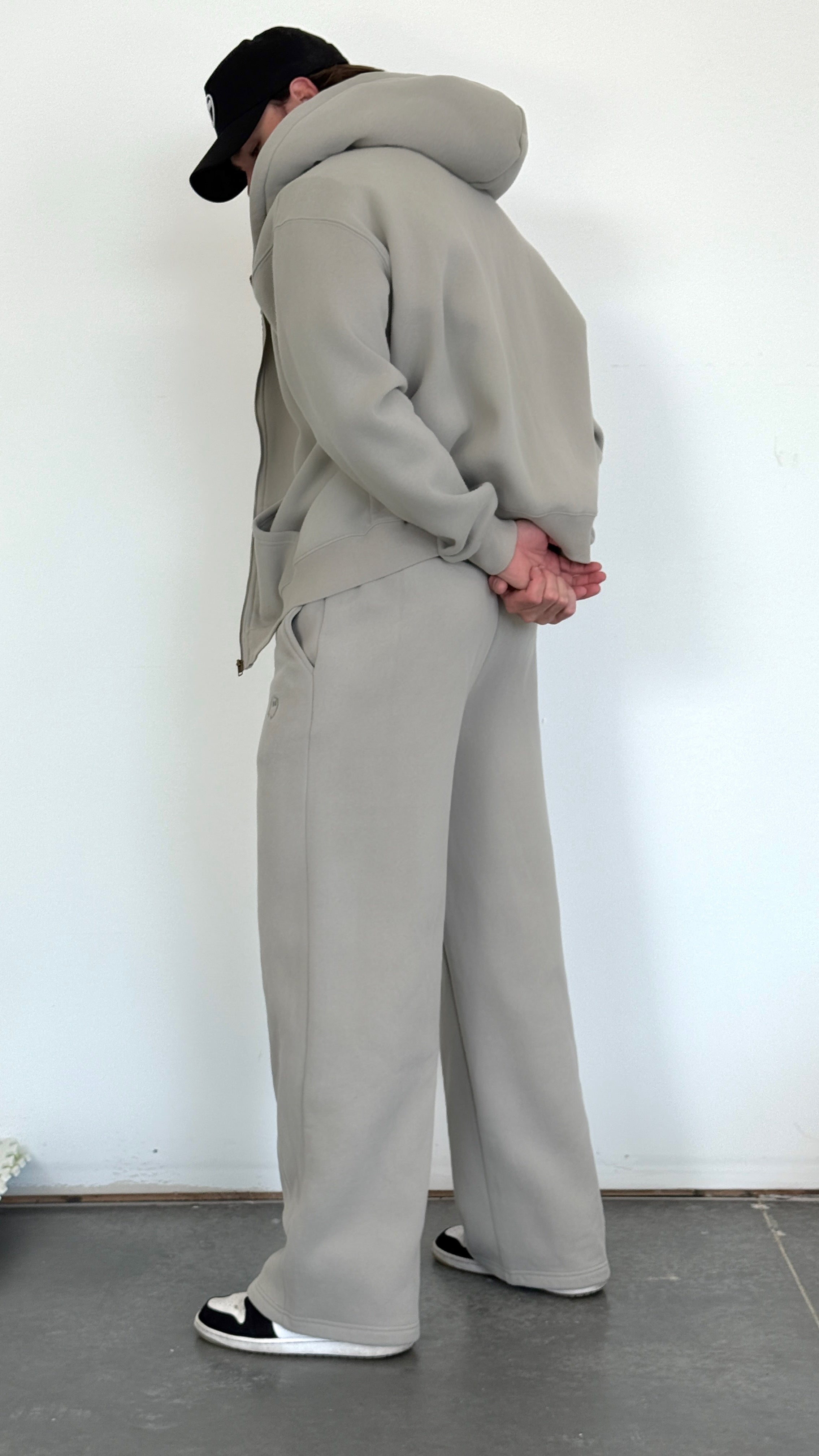 Person wearing a gray tracksuit standing against a white wall.
