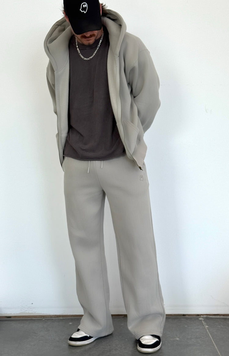 Person wearing a gray hoodie, gray pants, and black cap against a white wall.