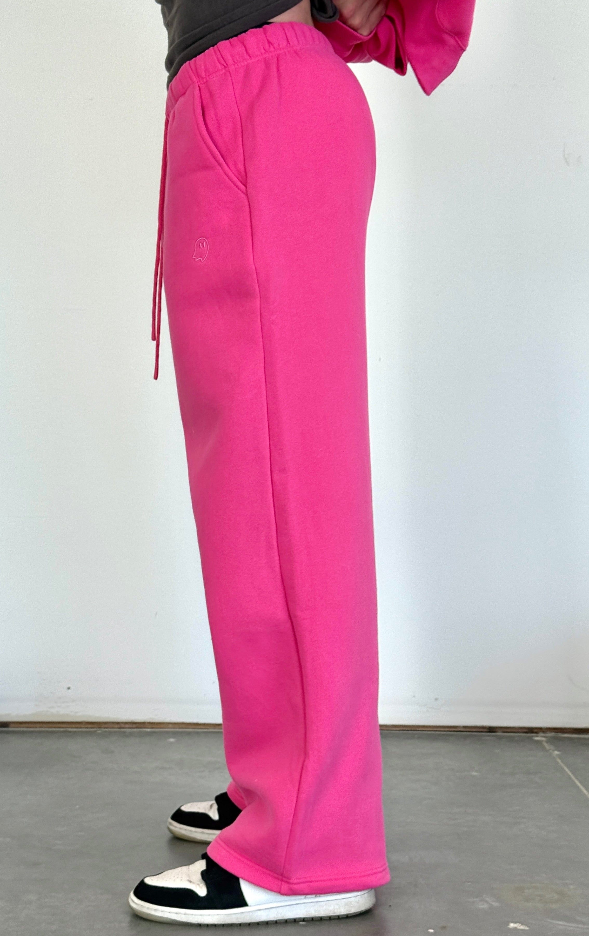 Person wearing bright pink pants and black and white shoes on a plain background