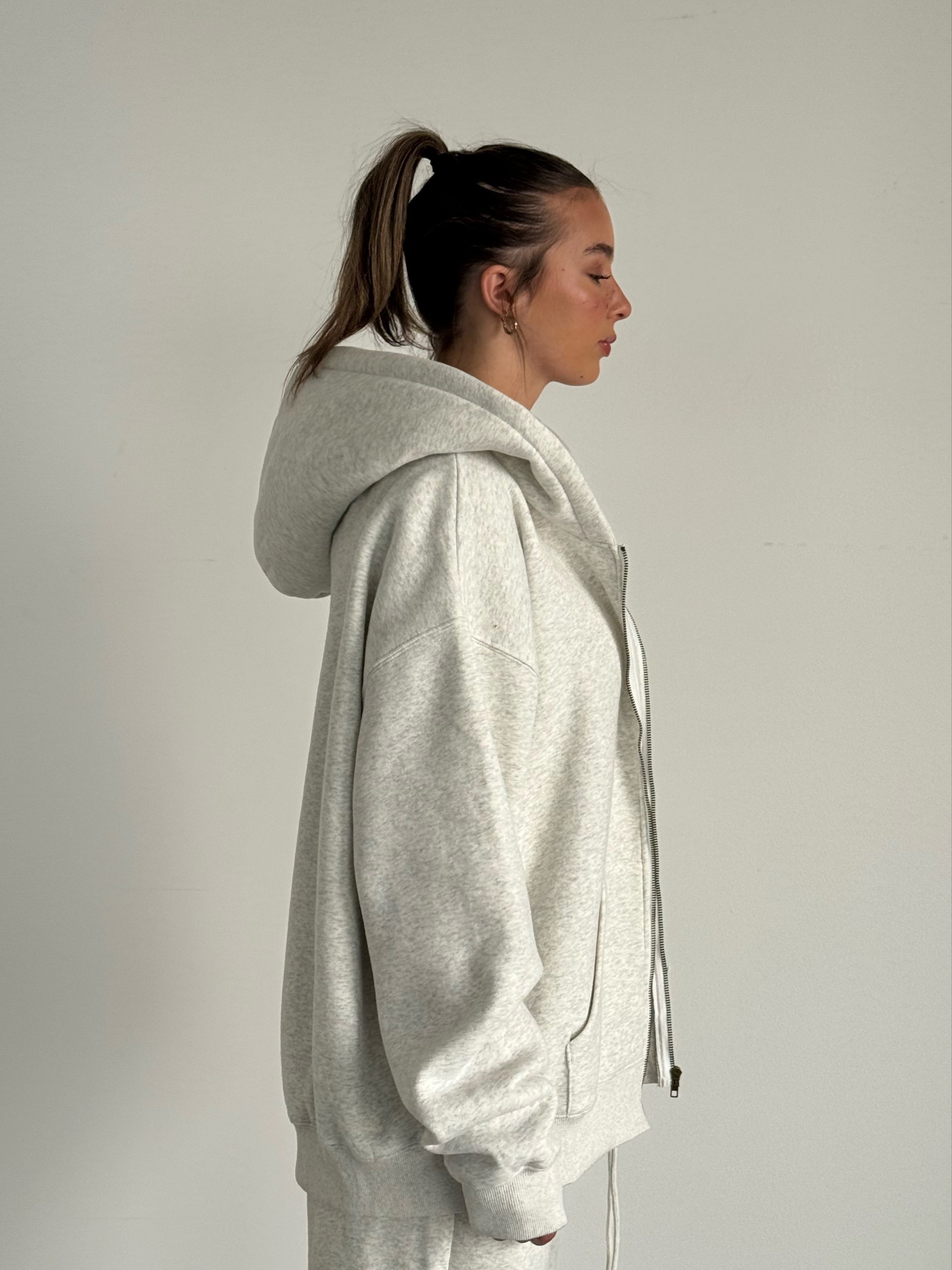 Person wearing a light gray hoodie and pants against a plain background