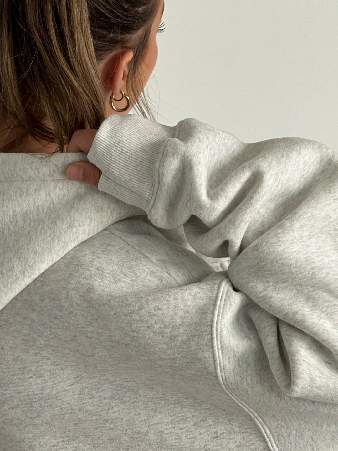 Person wearing a gray hoodie from behind on a plain background