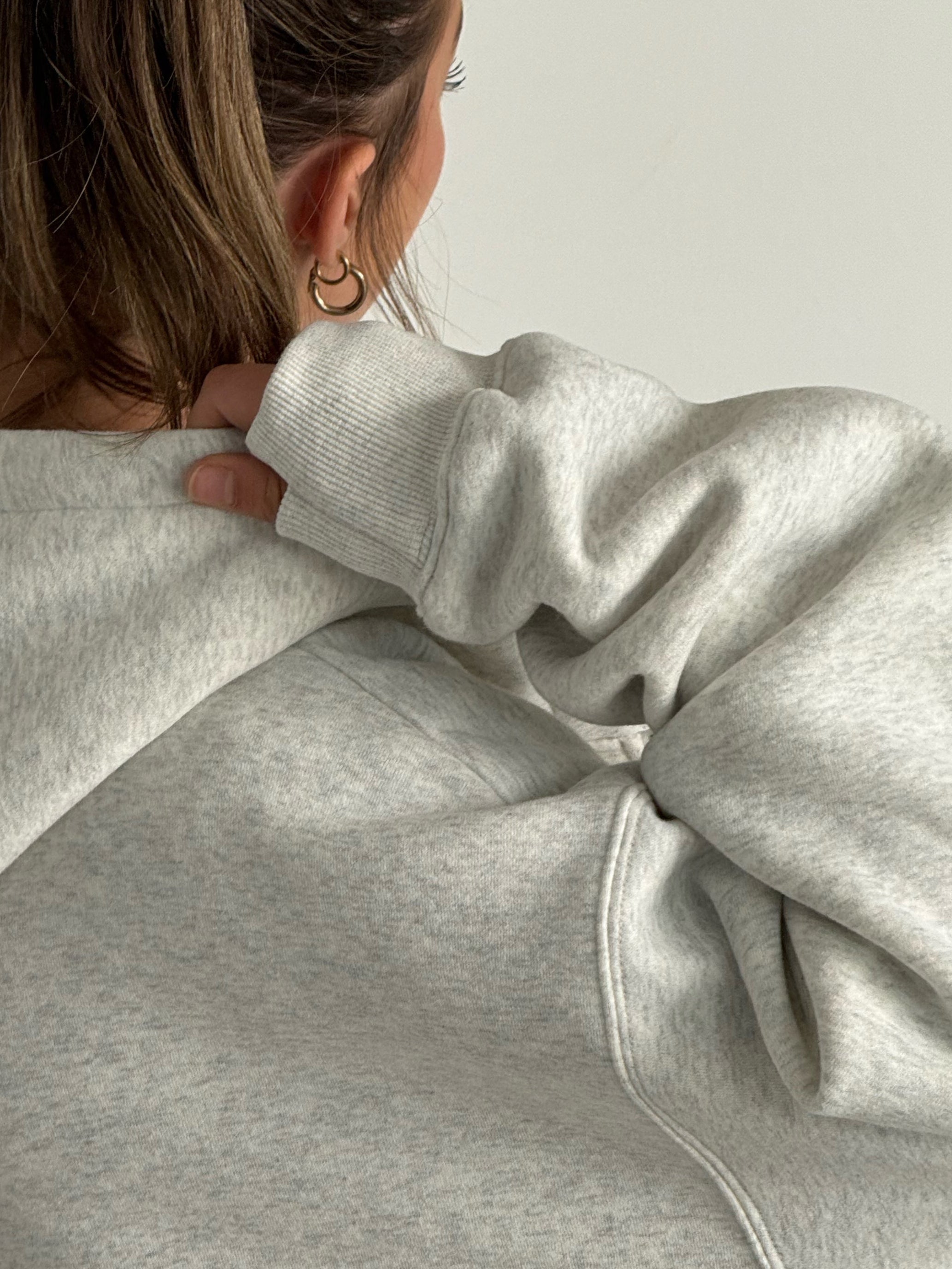 Person wearing a gray hoodie from behind on a plain background
