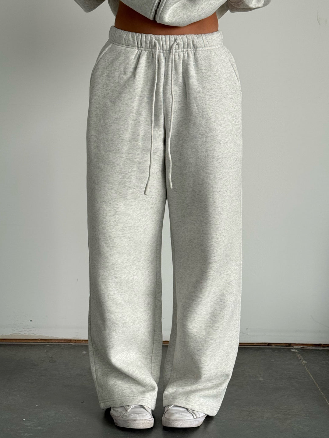 Person wearing gray sweatpants and a matching hoodie against a plain background