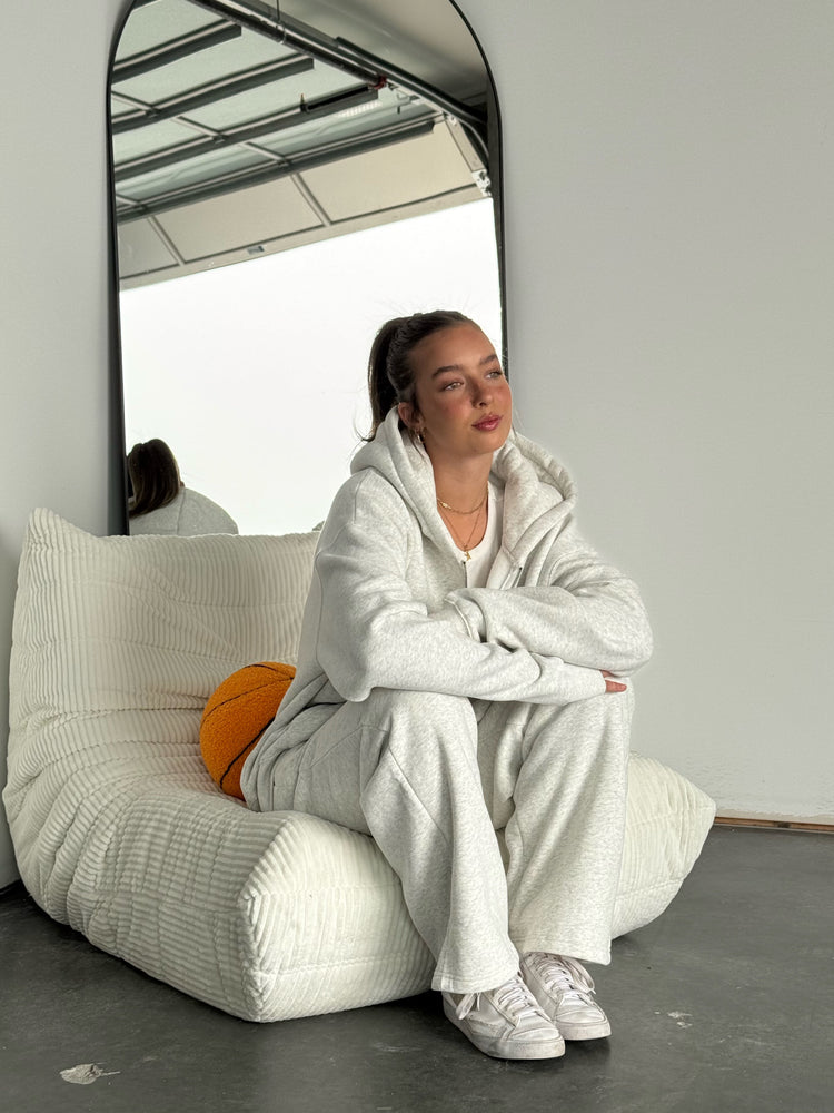 Person sitting on a white bean bag chair wearing a white outfit in a minimalistic room.