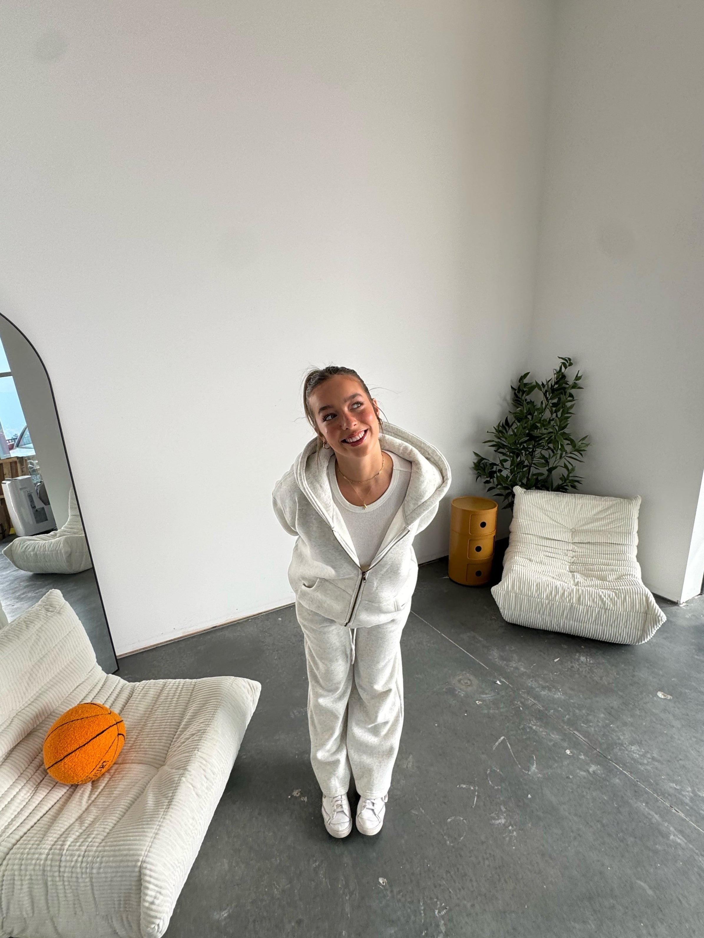 Person in a white outfit standing in a modern room with minimal furniture.