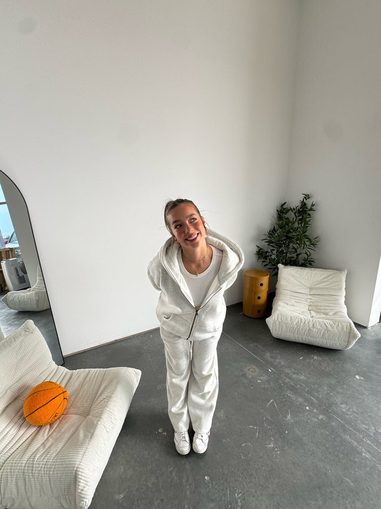 Person in a white outfit standing in a modern room with minimal furniture.