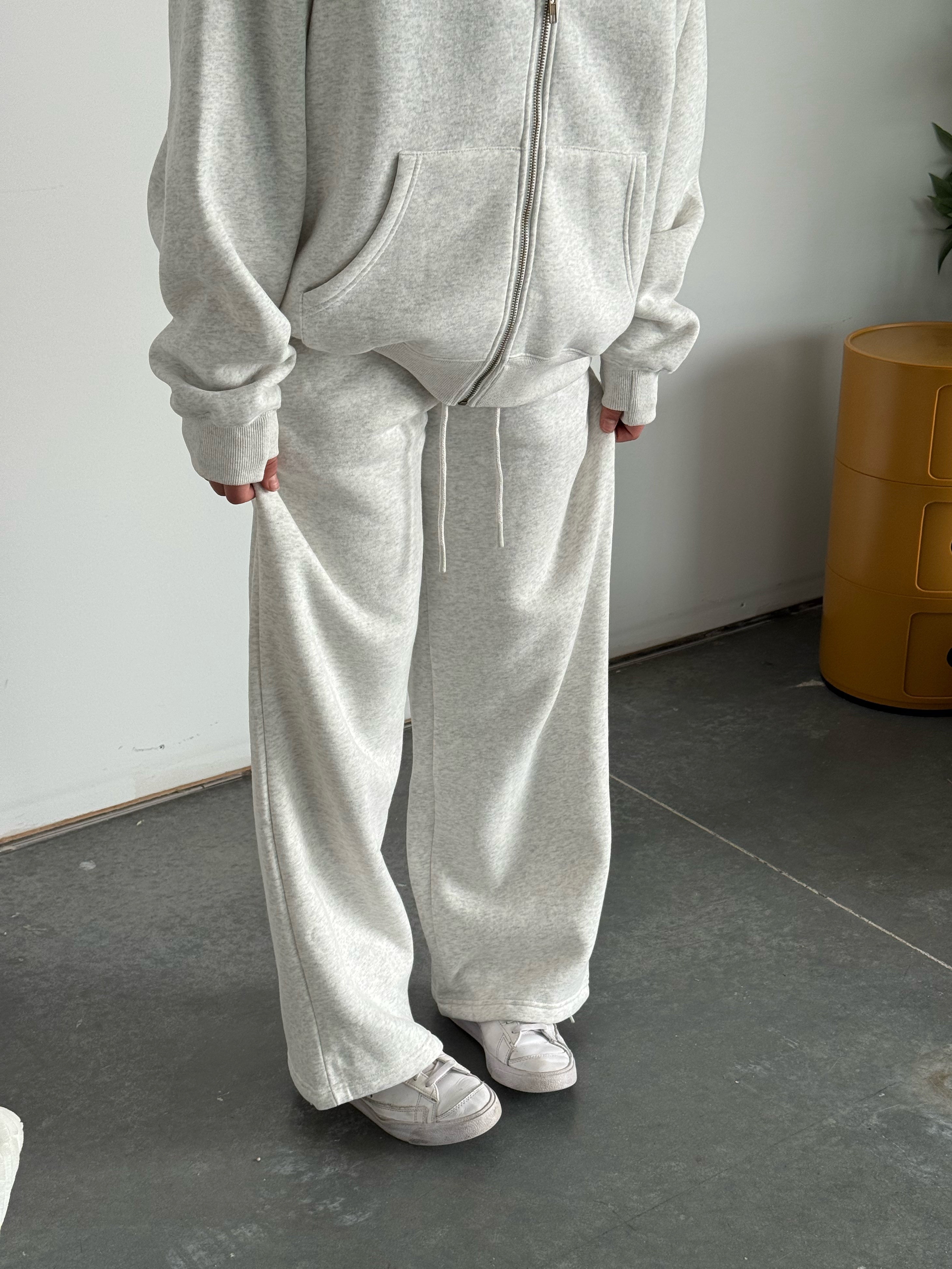 Person wearing a gray tracksuit standing in a minimal indoor setting.
