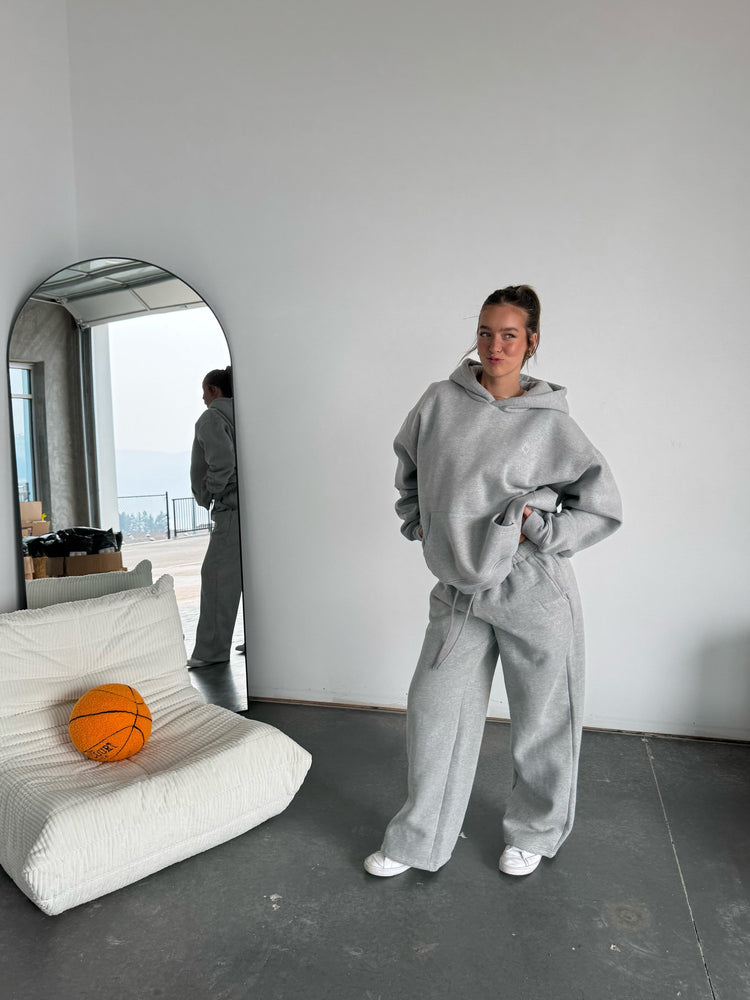 Person in gray hoodie and pants standing in a minimalistic room with a basketball and white cushion.