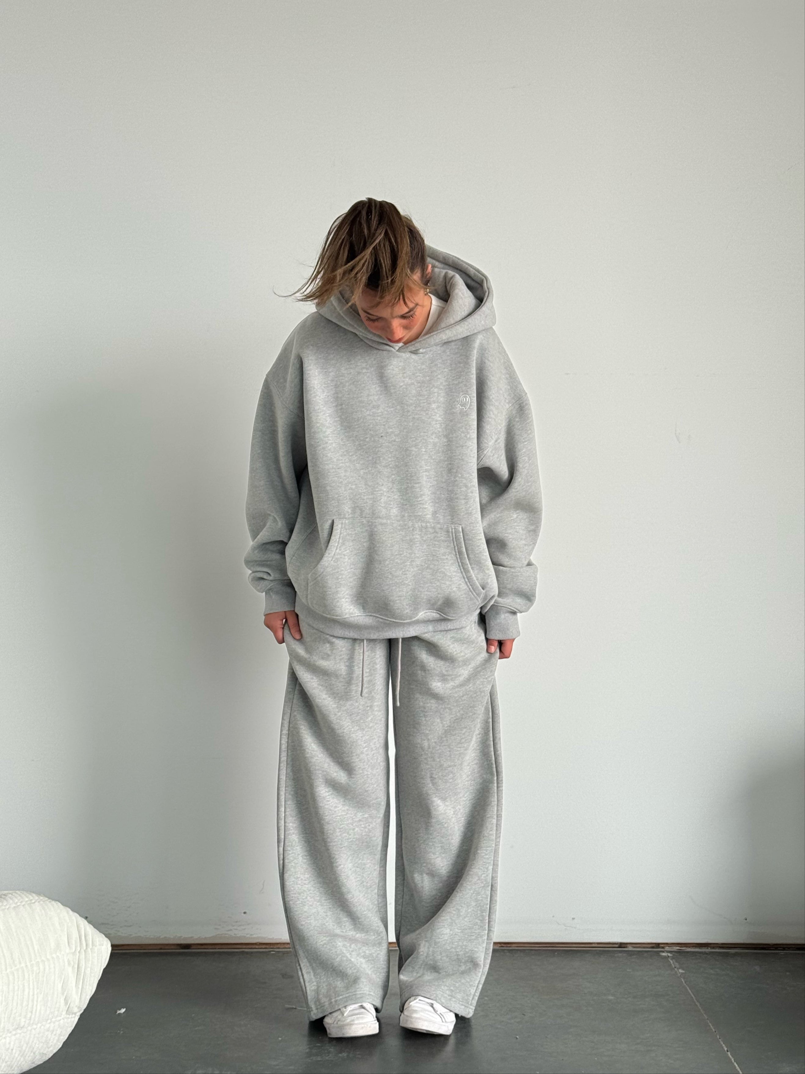 Person wearing a gray tracksuit standing against a plain white wall.