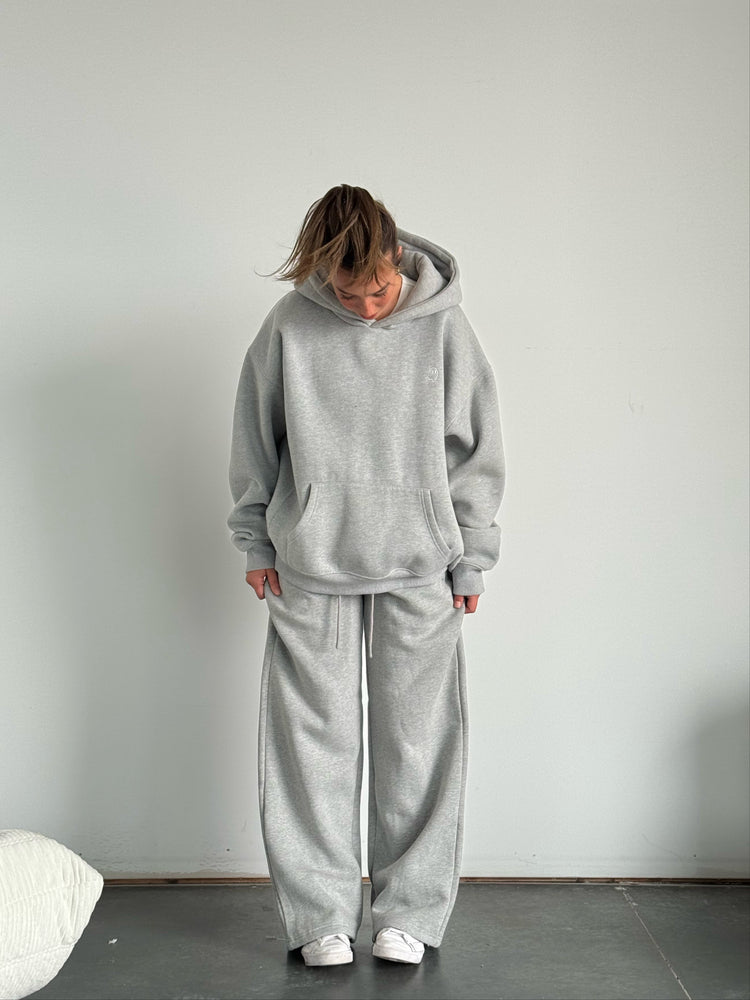 Person wearing a gray tracksuit standing against a plain white wall.