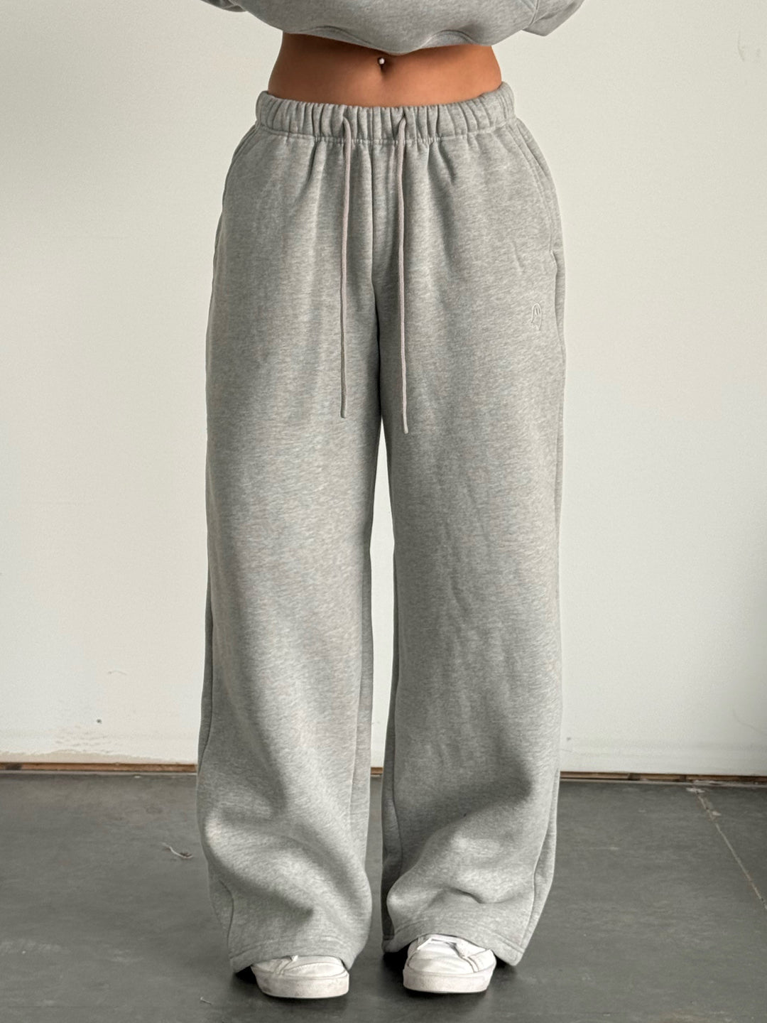 Person wearing a gray hoodie and wide-leg pants standing against a plain background