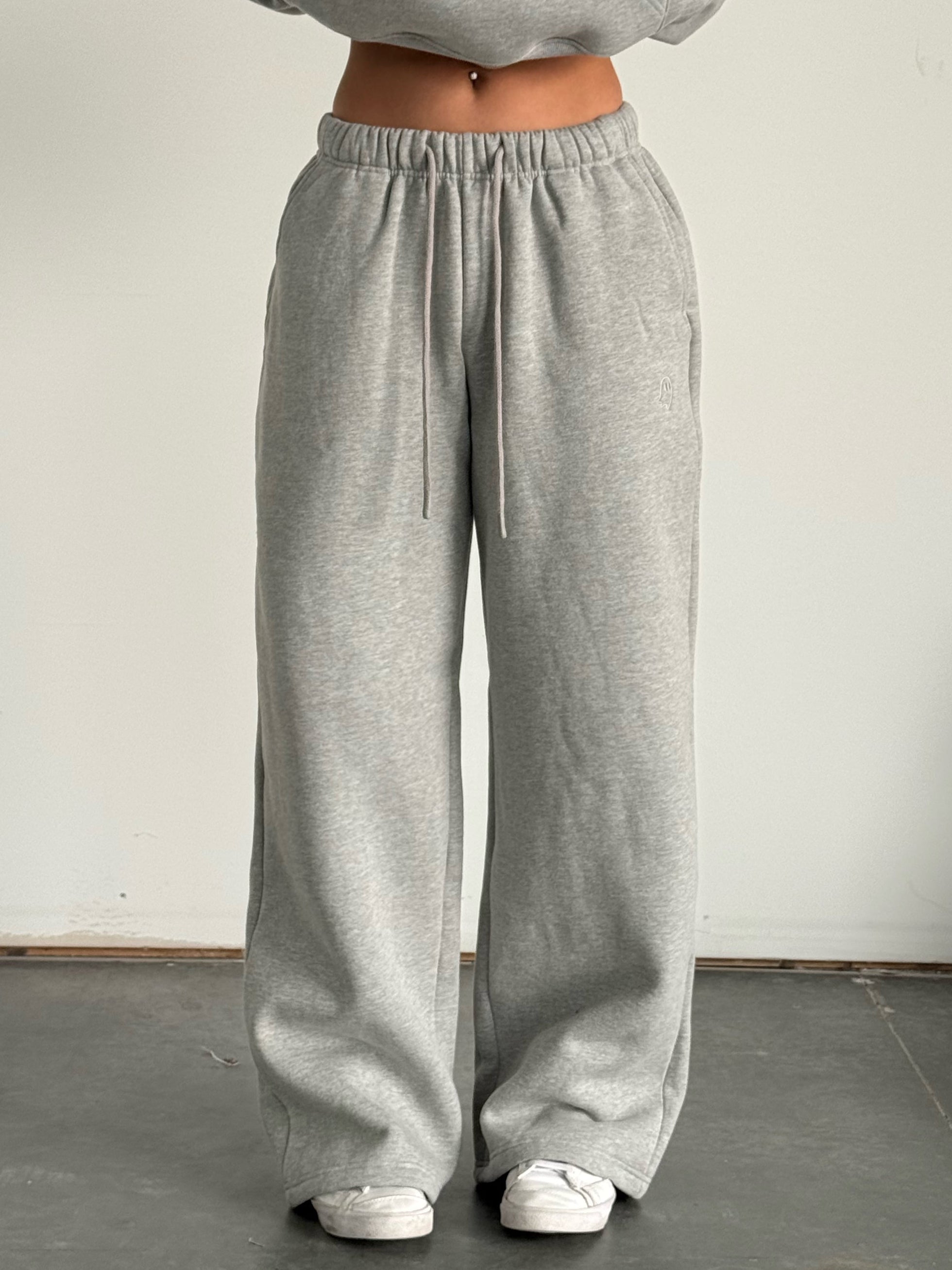 Person wearing a gray hoodie and wide-leg pants standing against a plain background