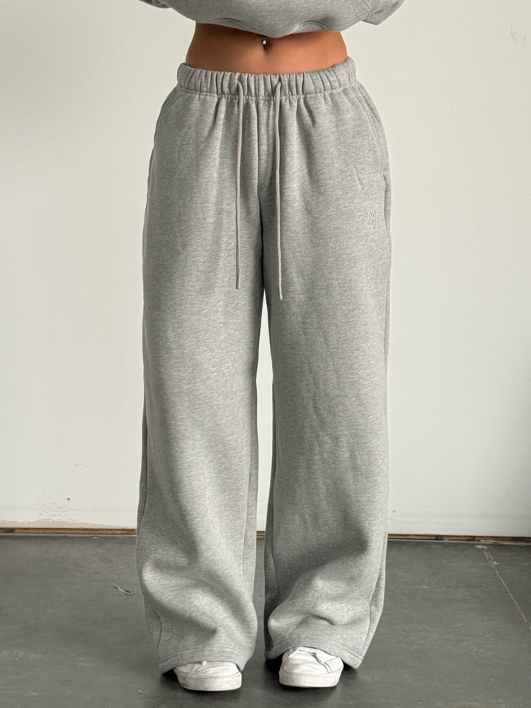 Person wearing a gray hoodie and wide-leg pants standing against a plain background