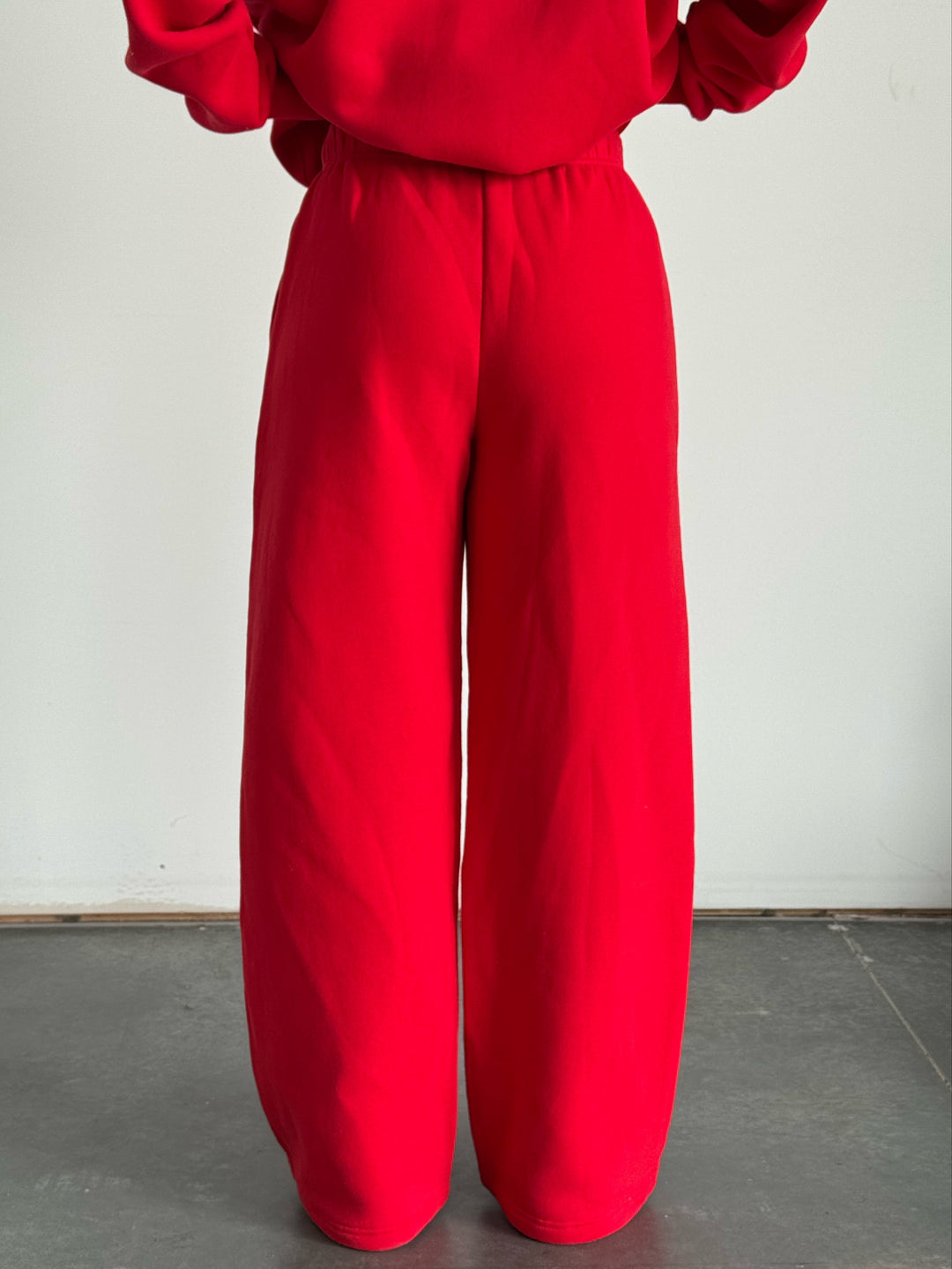 Person wearing a red outfit with wide-legged pants on a plain background