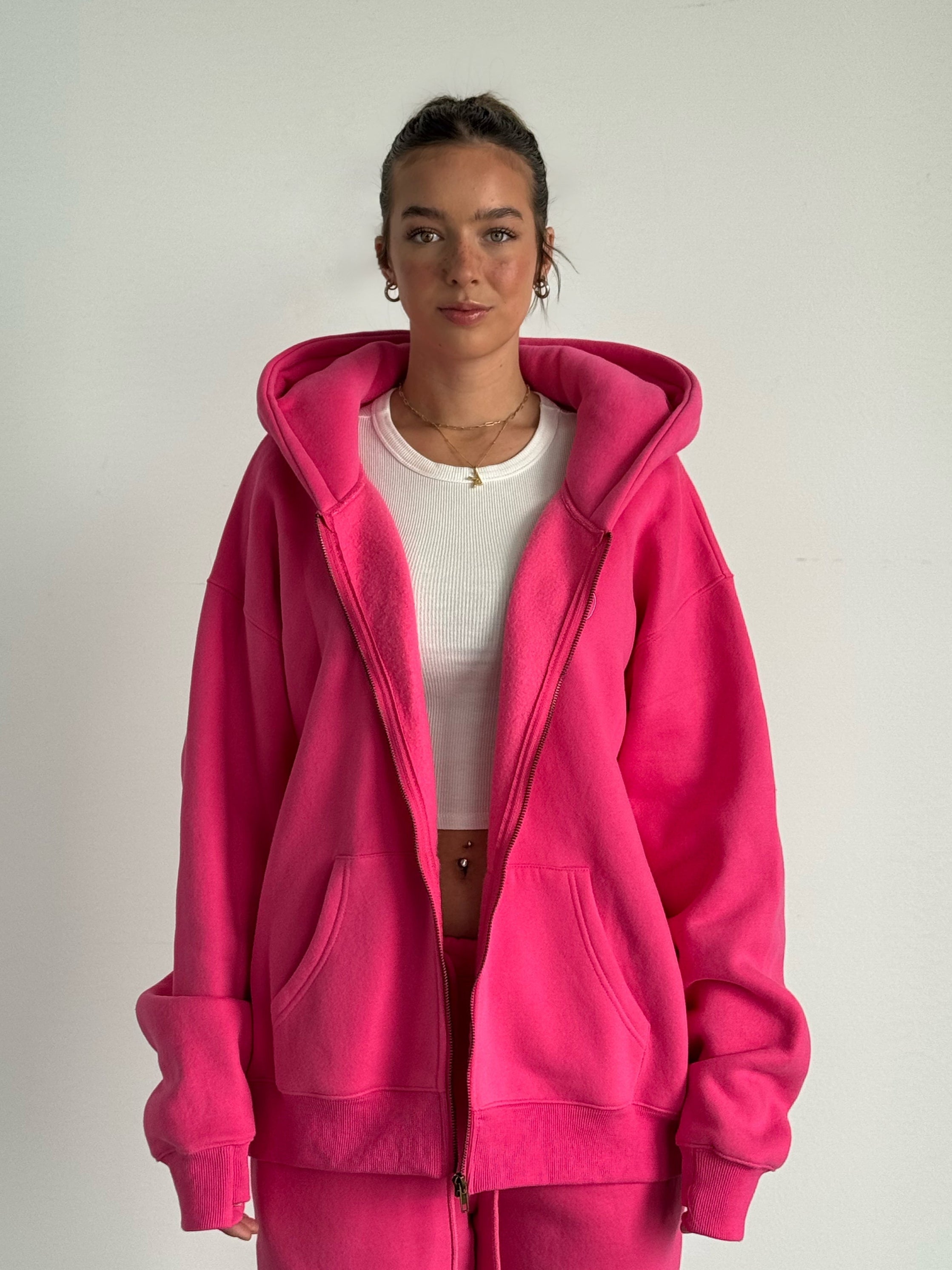 Person wearing a bright pink hoodie and pants on a plain background