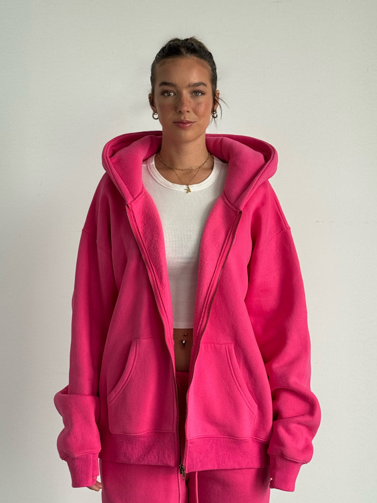 Person wearing a bright pink hoodie and pants on a plain background