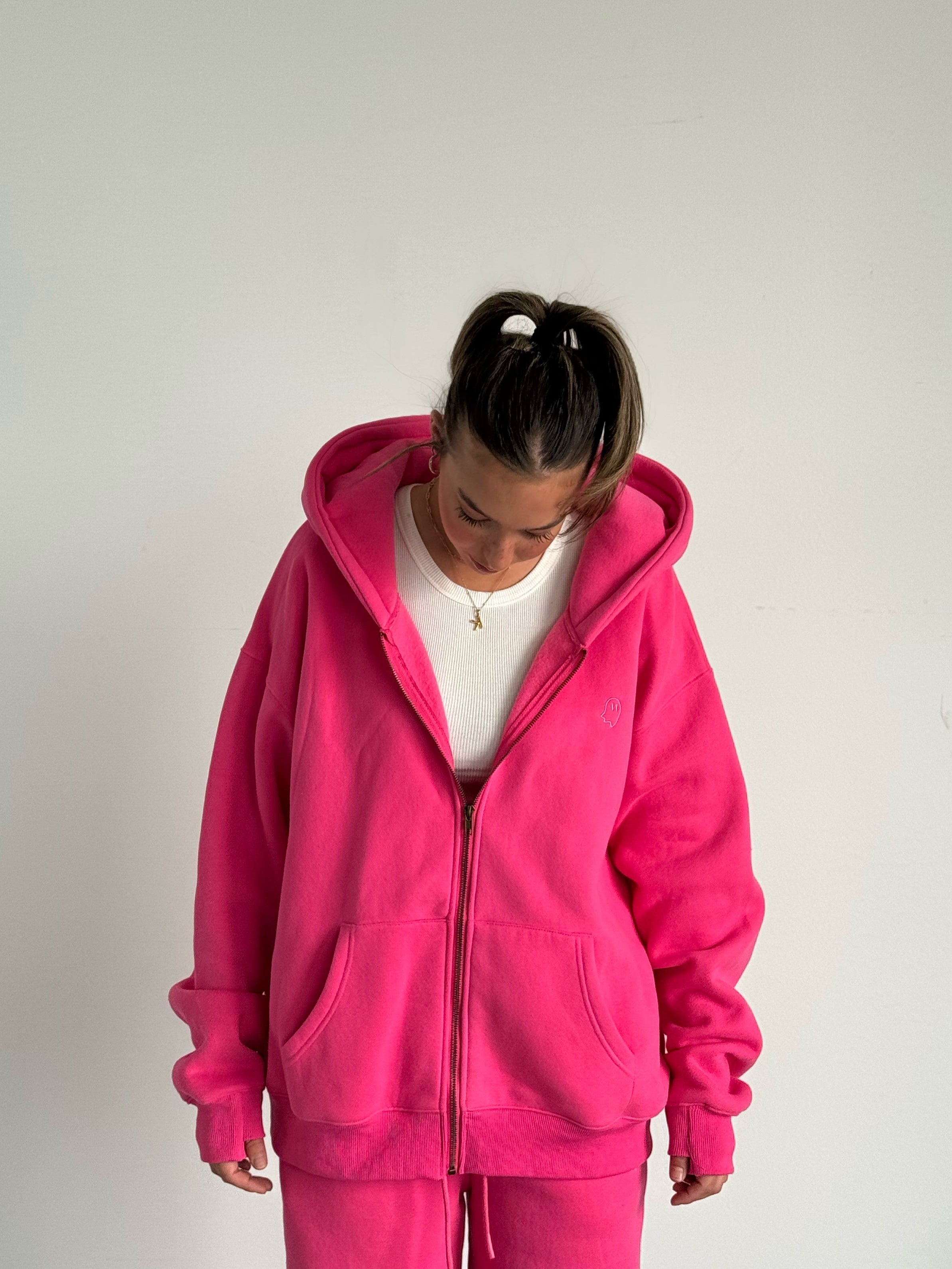 Person wearing a bright pink hoodie and pants on a plain background