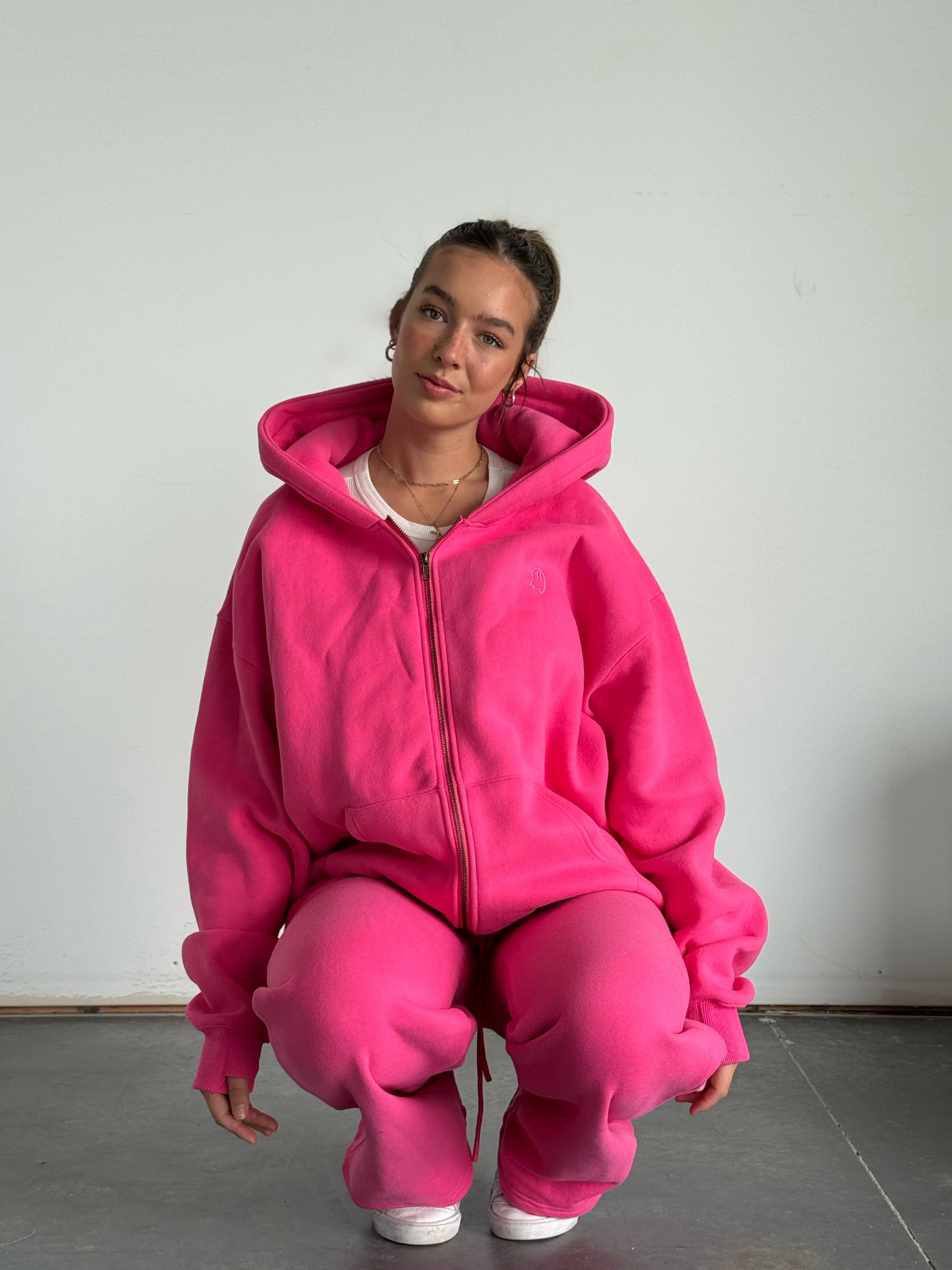 Person wearing a bright pink hoodie and pants sitting on the floor against a plain background