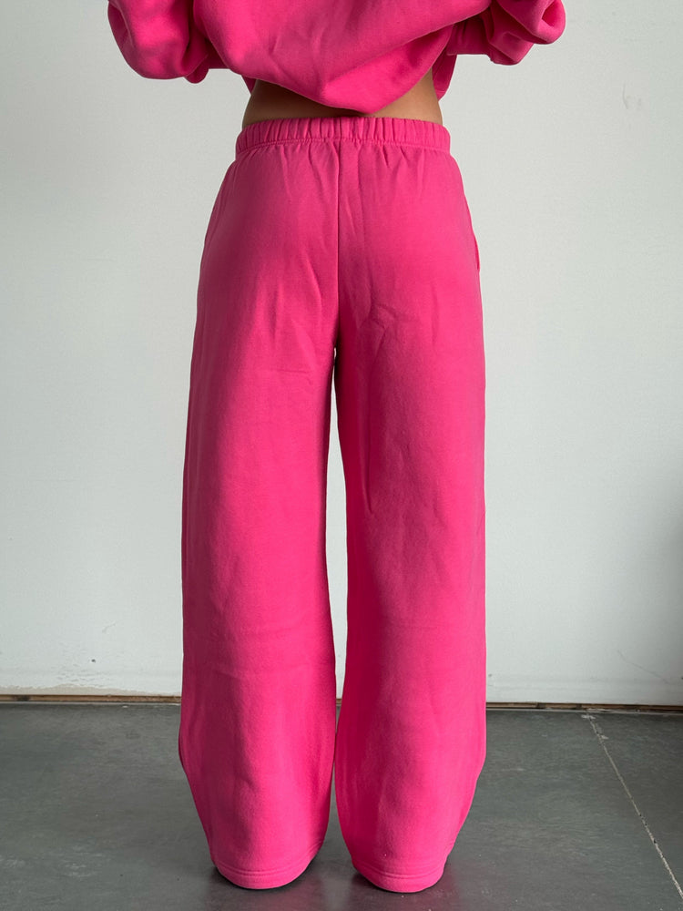 Person wearing a bright pink outfit with a matching top and pants against a plain background
