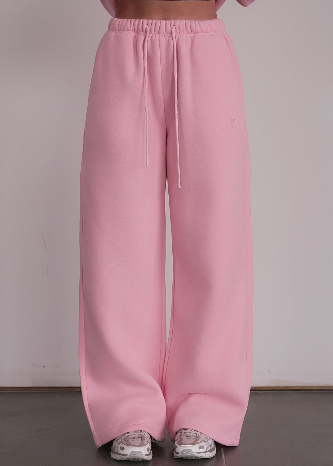 Person wearing a pink outfit with wide-leg pants and a cropped top against a plain background