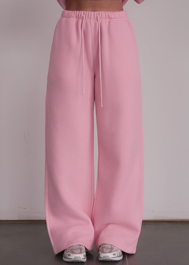 Person wearing a pink outfit with wide-leg pants and a cropped top against a plain background