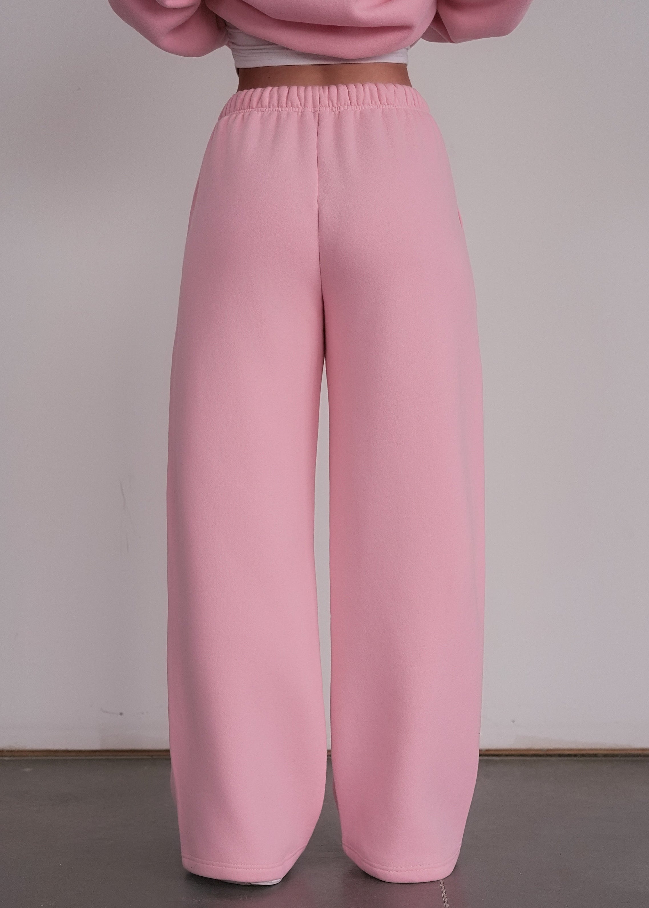 Person wearing pink sweatpants and a cropped pink sweater against a plain background