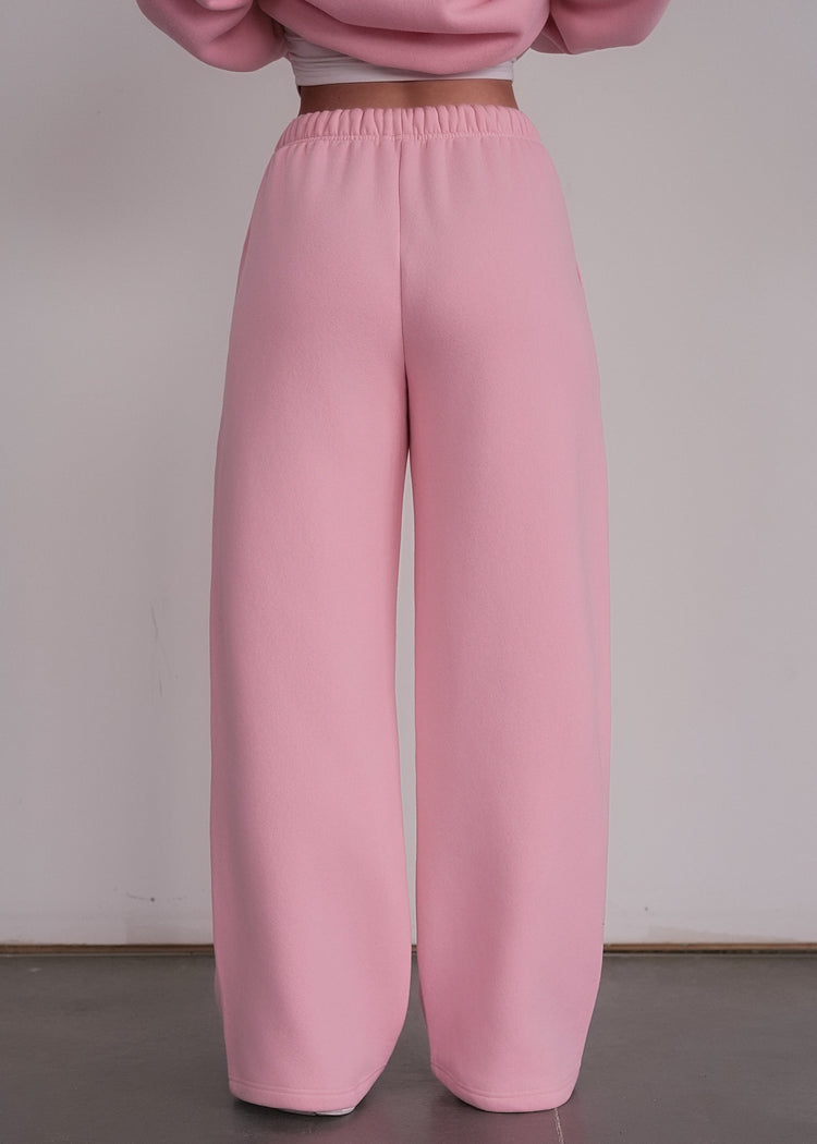 Person wearing pink sweatpants and a cropped pink sweater against a plain background