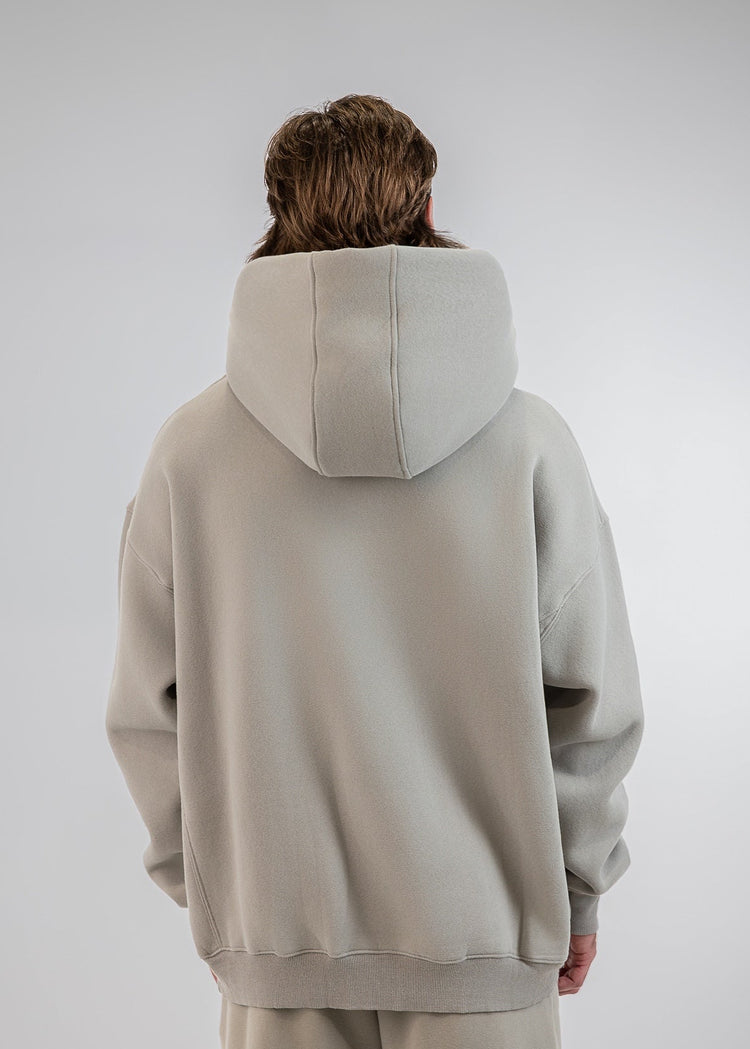A person viewed from behind wearing an oversized light beige hoodie and matching sweatpants against a plain light gray studio background.