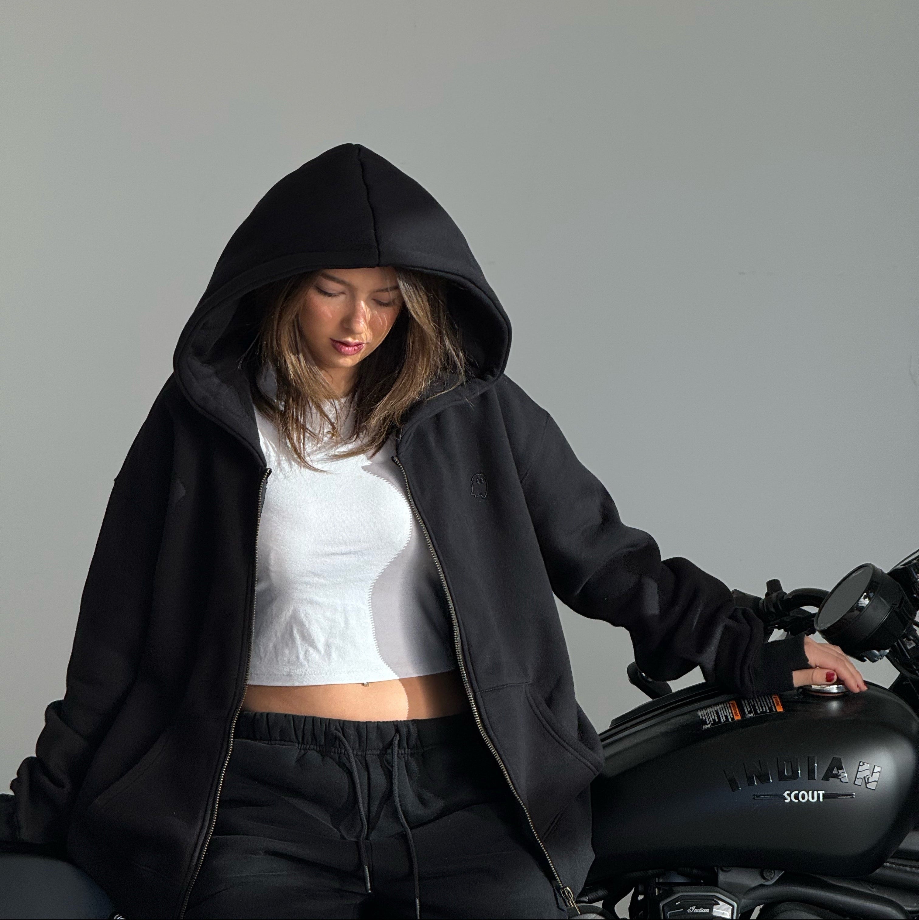 Person wearing a black hoodie and white top sitting next to a motorcycle on a gray background