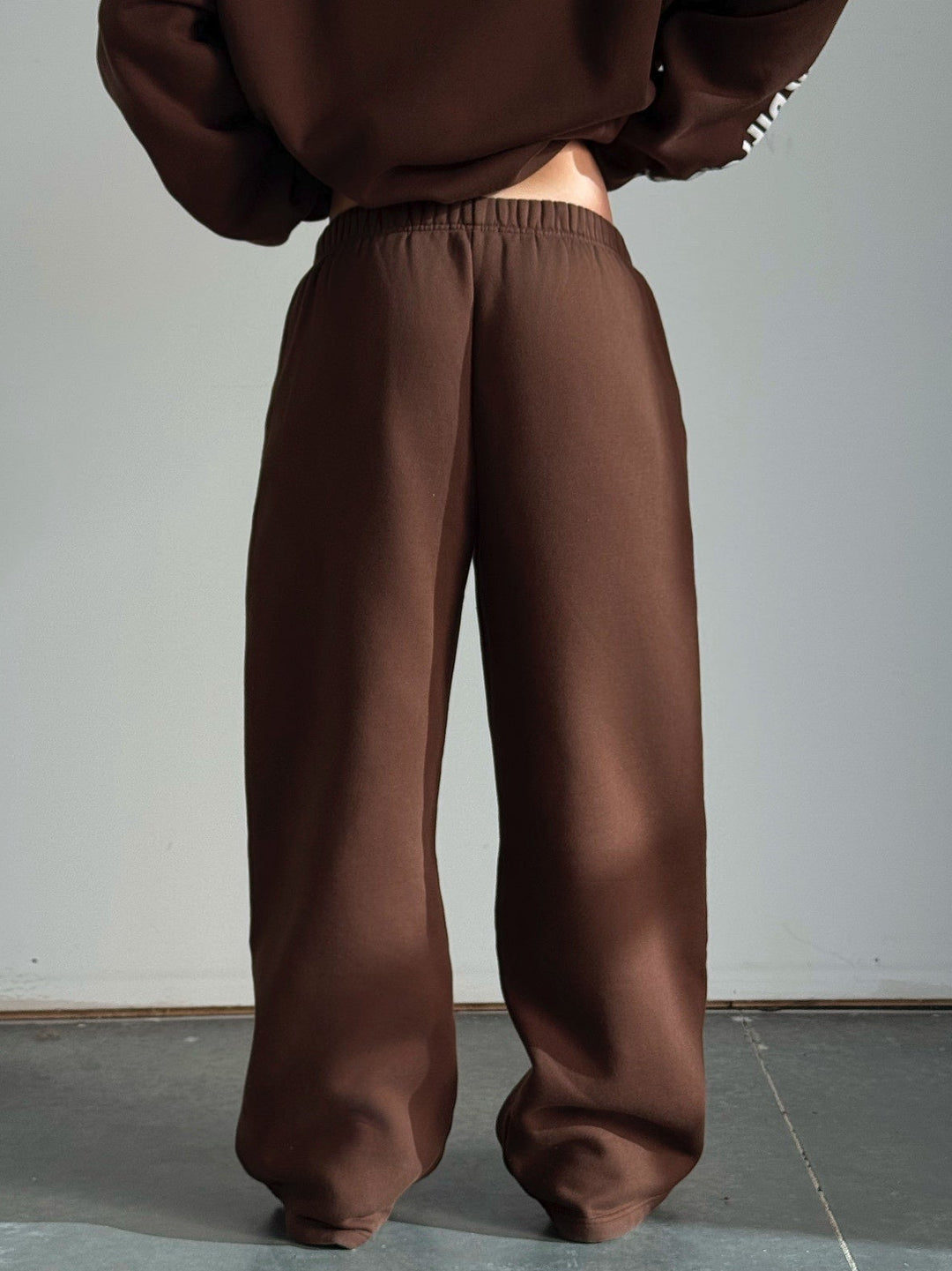 Person wearing a brown hoodie and pants against a plain background