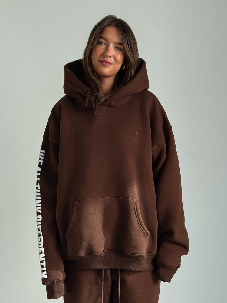 Person wearing a brown hoodie and pants with a visible brand logo on a plain background