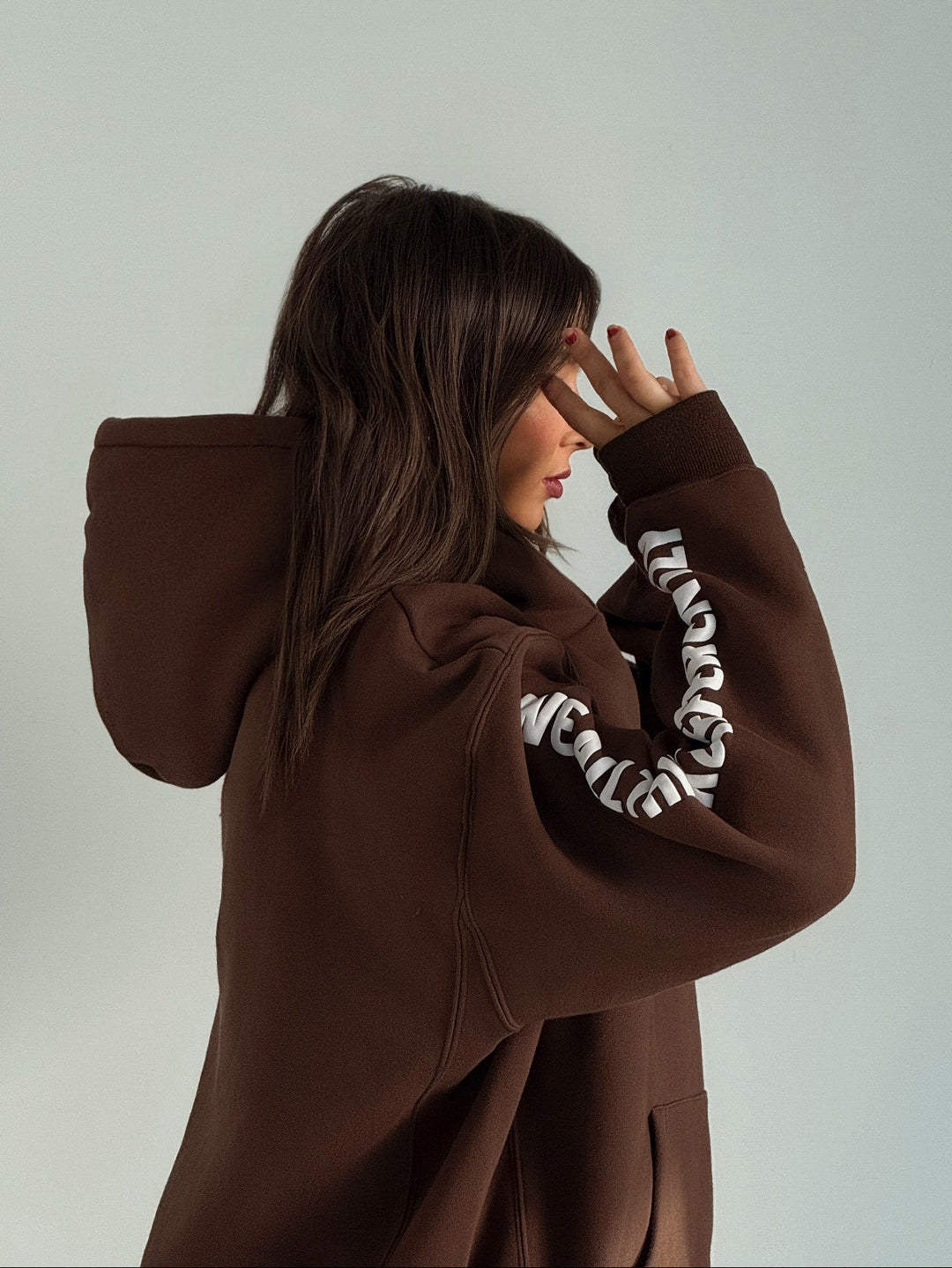 Person wearing a brown hoodie with white text on sleeves against a plain background