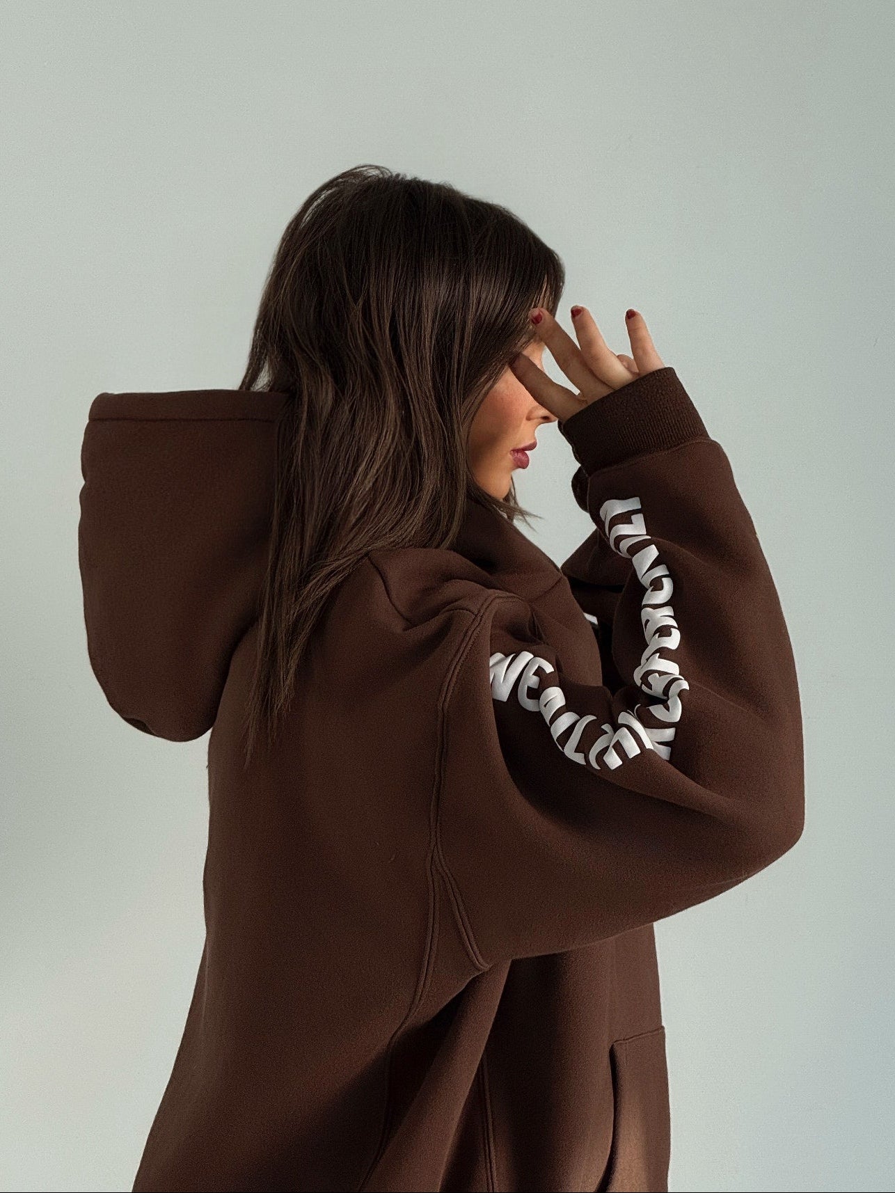 Person wearing a brown hoodie with white text on sleeves against a plain background