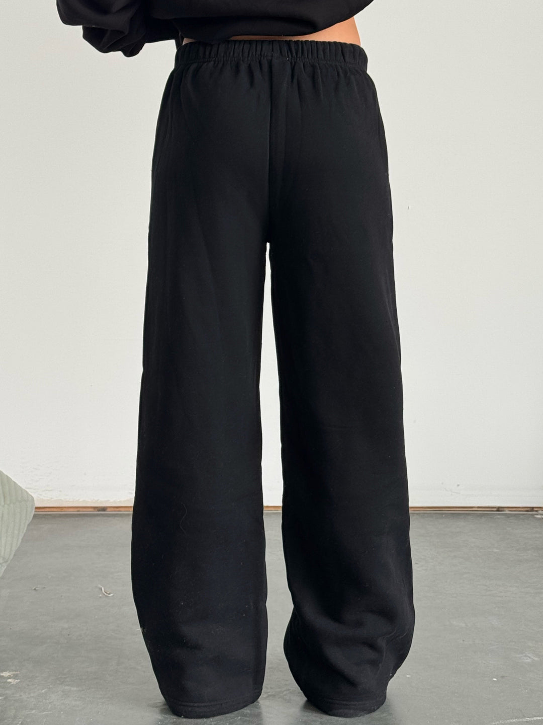 Person wearing a black hoodie and black wide-leg pants against a plain background