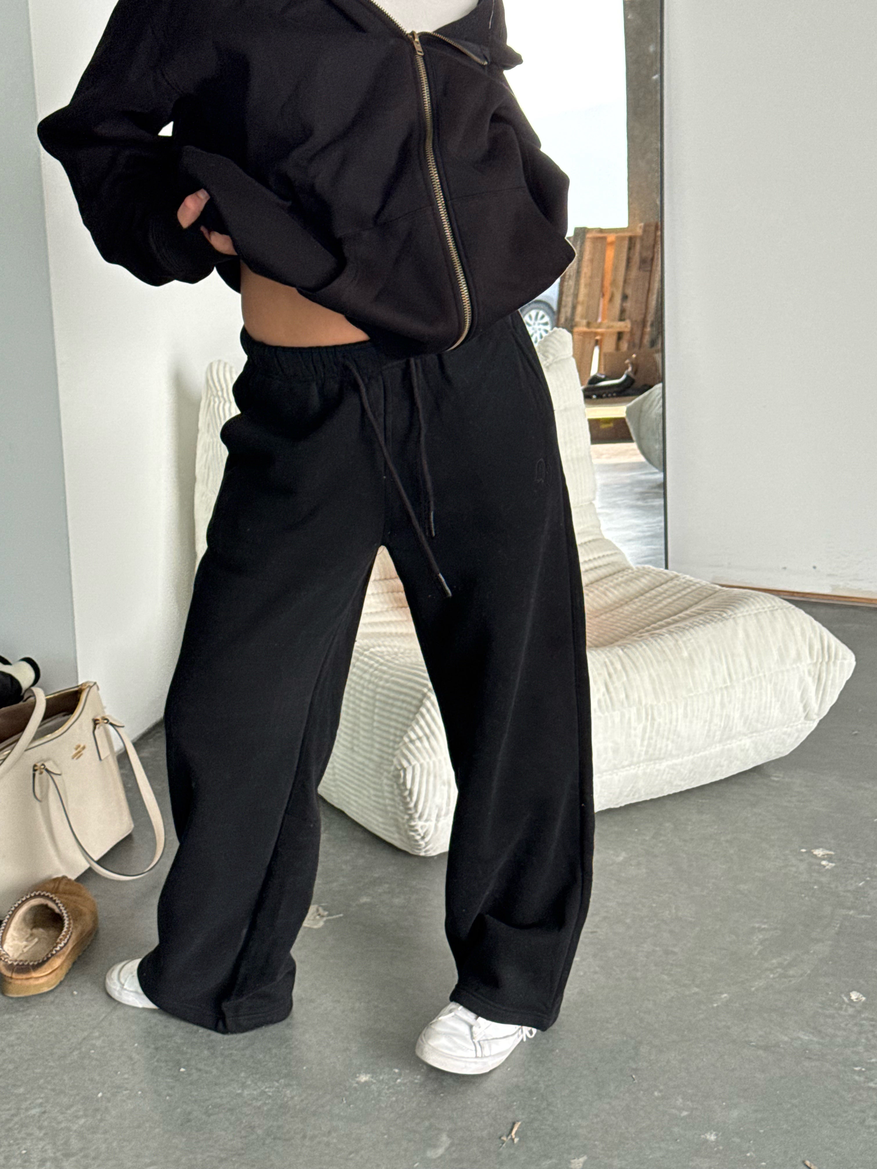 Person wearing a black tracksuit in a room with a mirror and pillows.