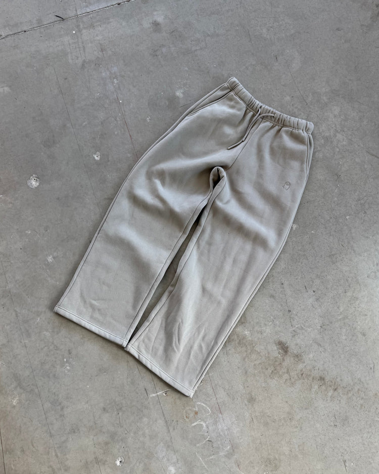 Grey sweatpants on a concrete floor with a person wearing white sneakers and light blue jeans.