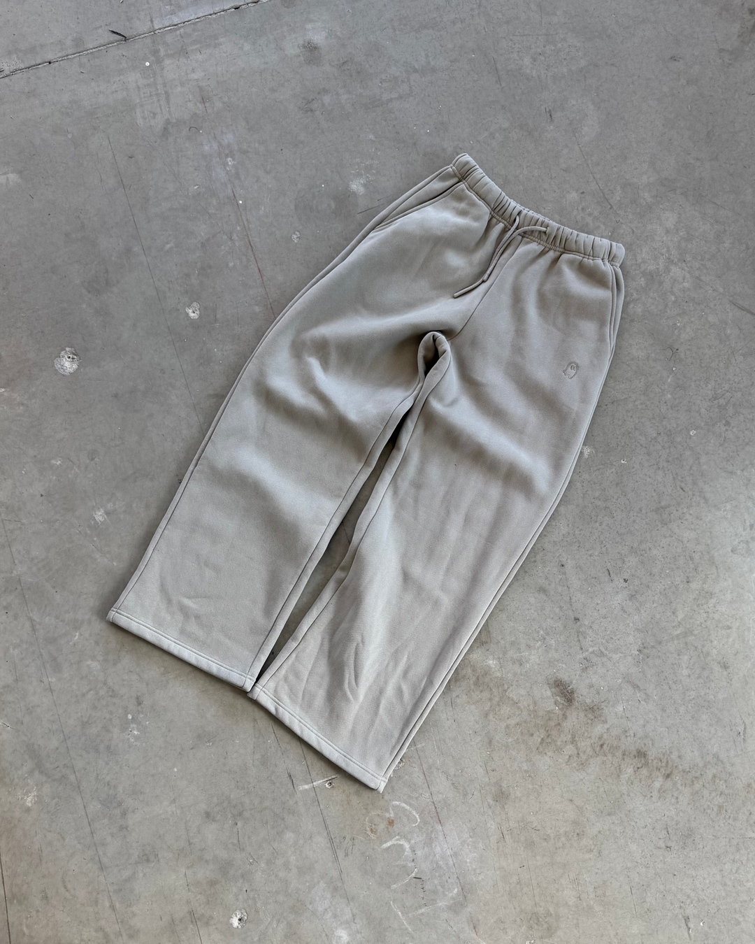 Grey sweatpants on a concrete floor with a person wearing white sneakers and light blue jeans.