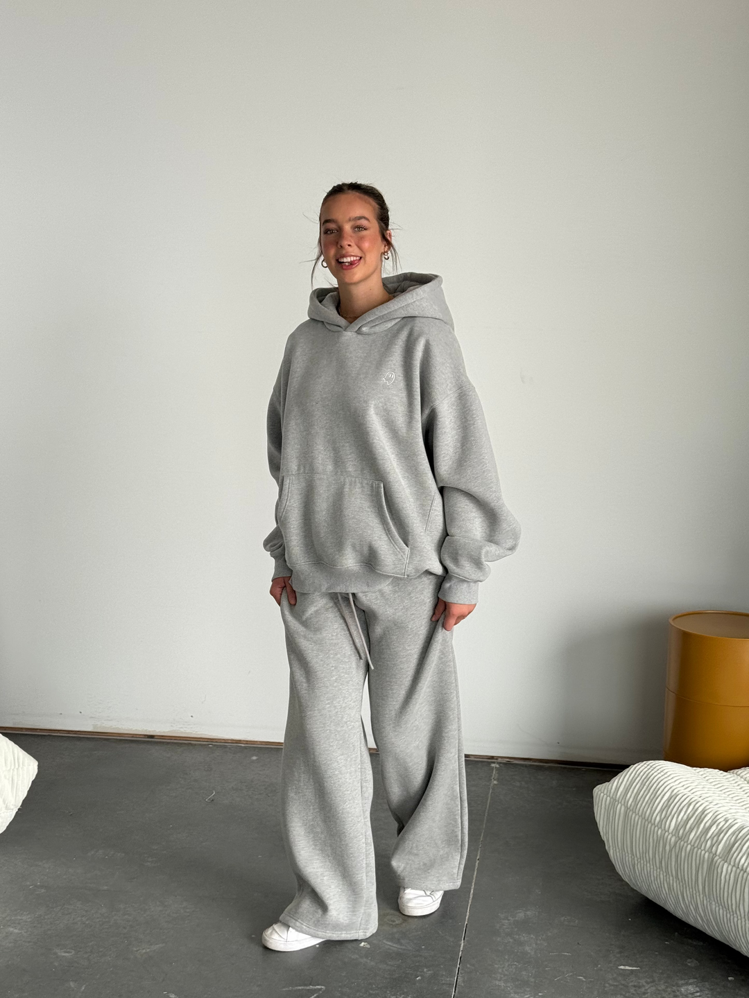 Person wearing a gray tracksuit standing in a minimalistic room with a white wall and gray floor.