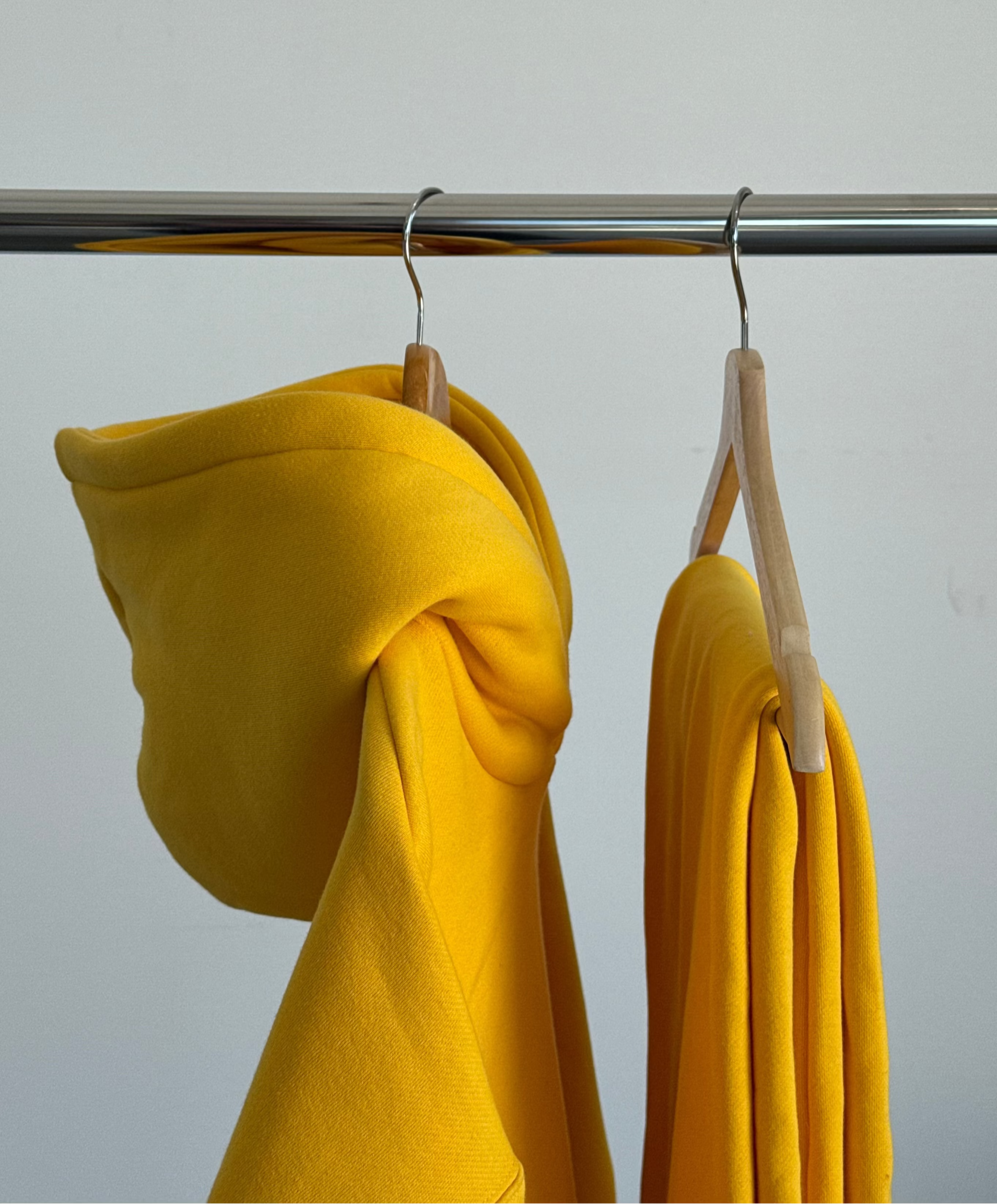 Yellow hoodie on a hanger against a plain background