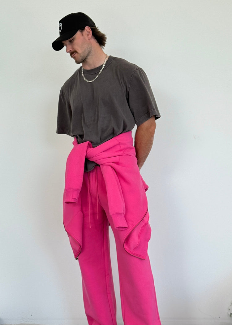 Person wearing a dark shirt, pink pants, and a black cap against a white wall.